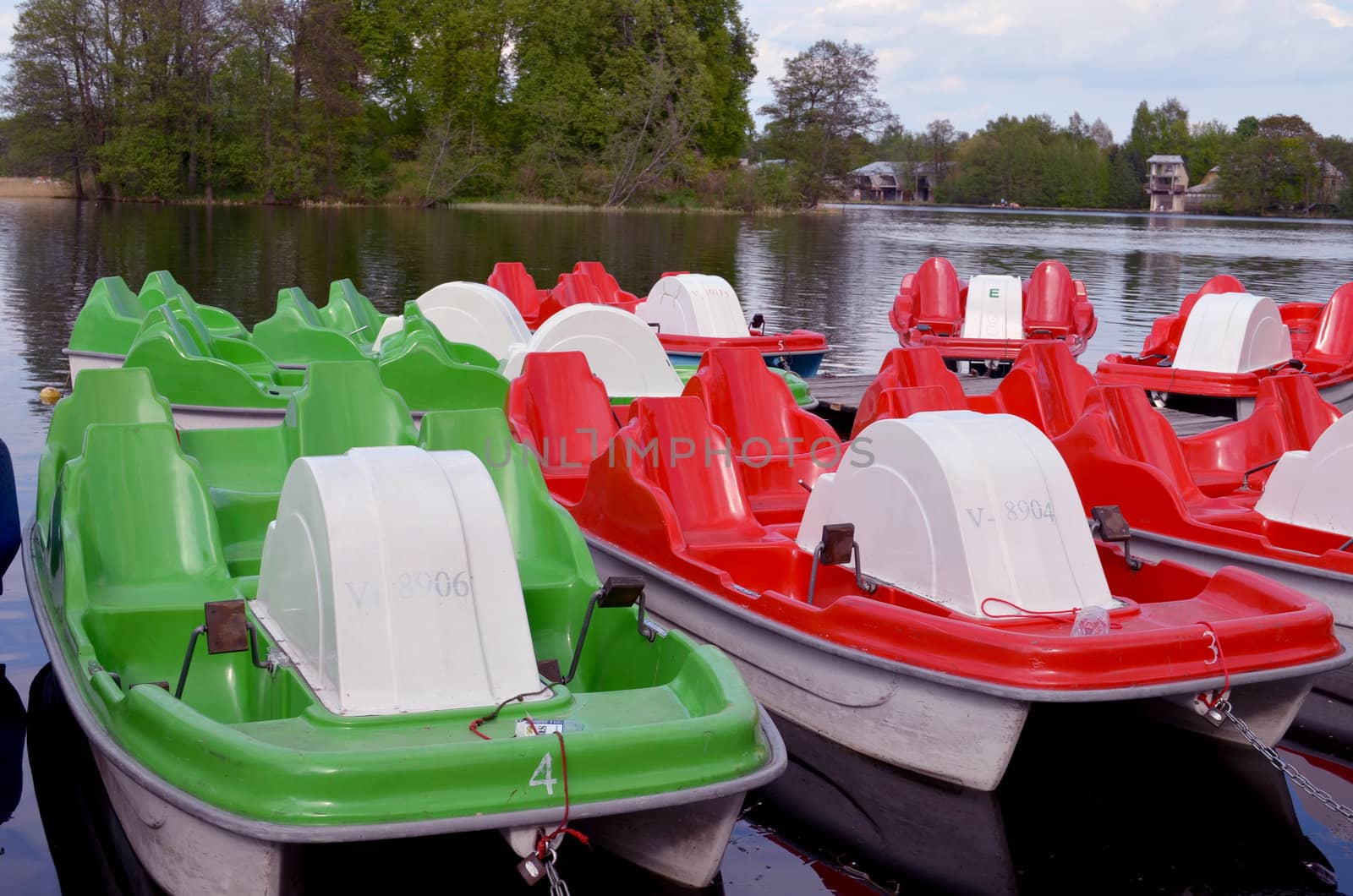 Water bicycles green and red locked at lake pier by sauletas