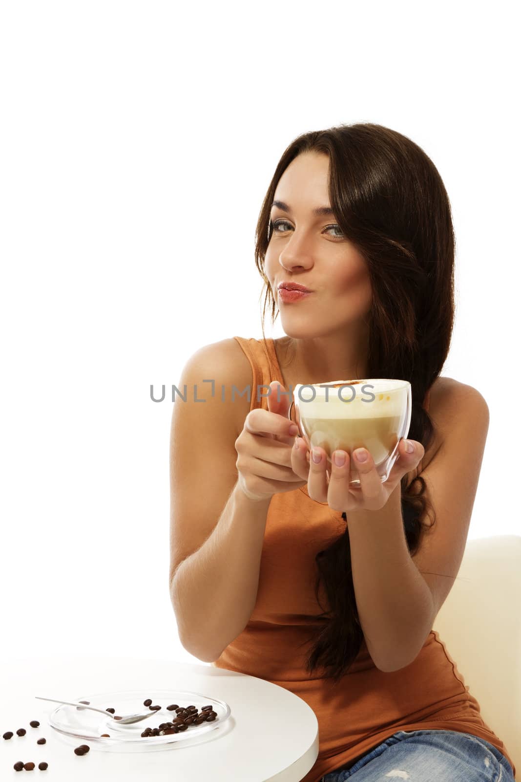young woman sitting at a table with cappuccino coffee making puss face on white background