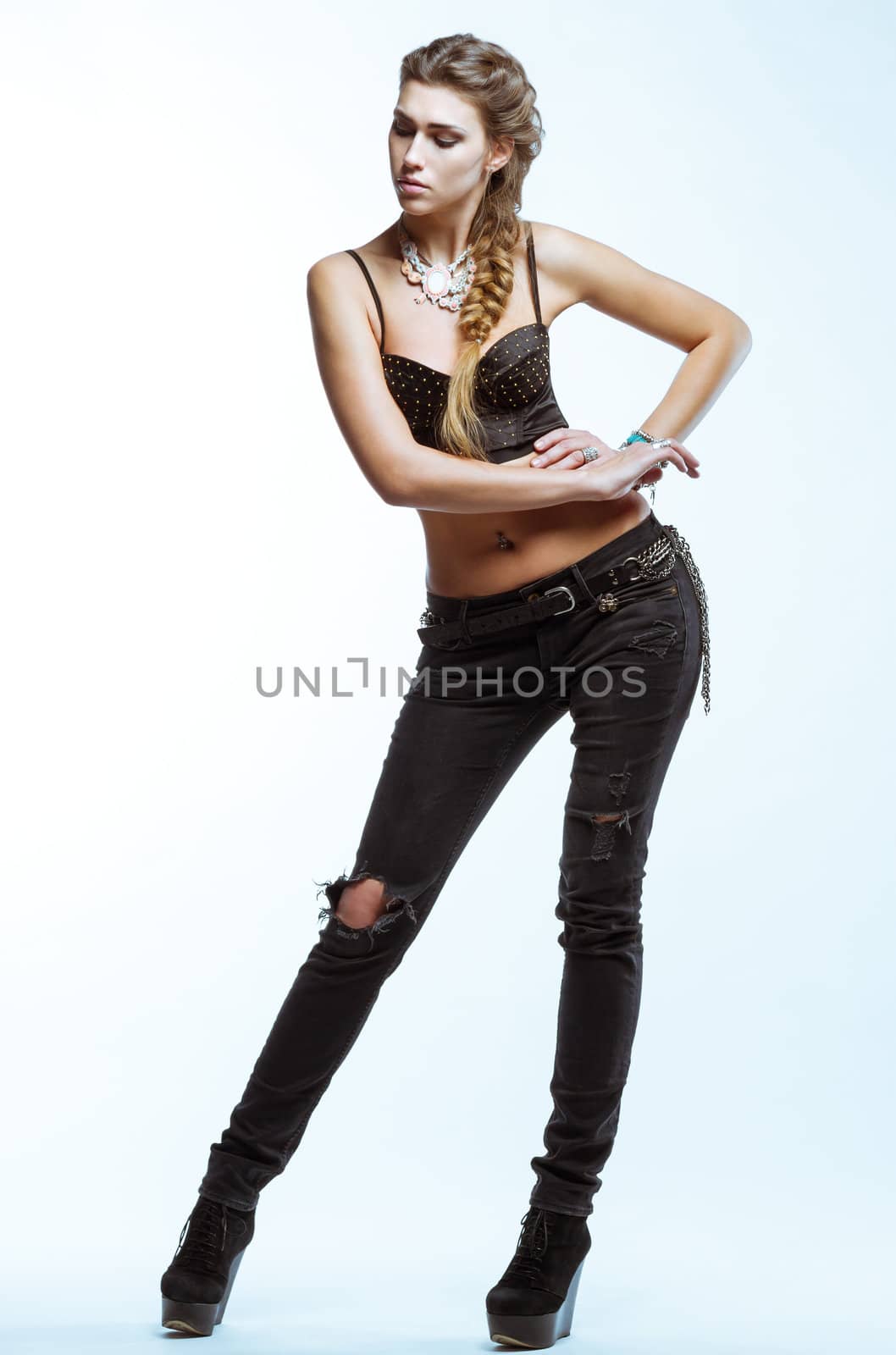 Young blond woman in black top and jeans posing on light backgro by vitmihailov