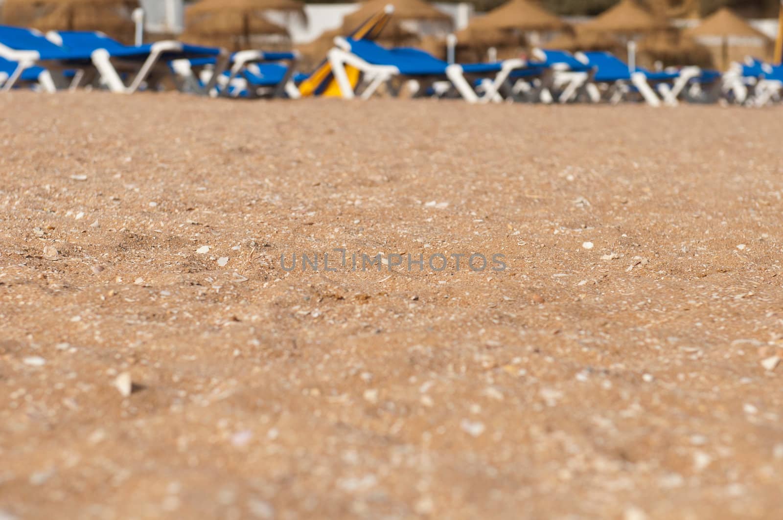 stunning beach sand with small shells on a very shallow DOF (plenty copy-space for your design, chairs and umbrellas at the background)