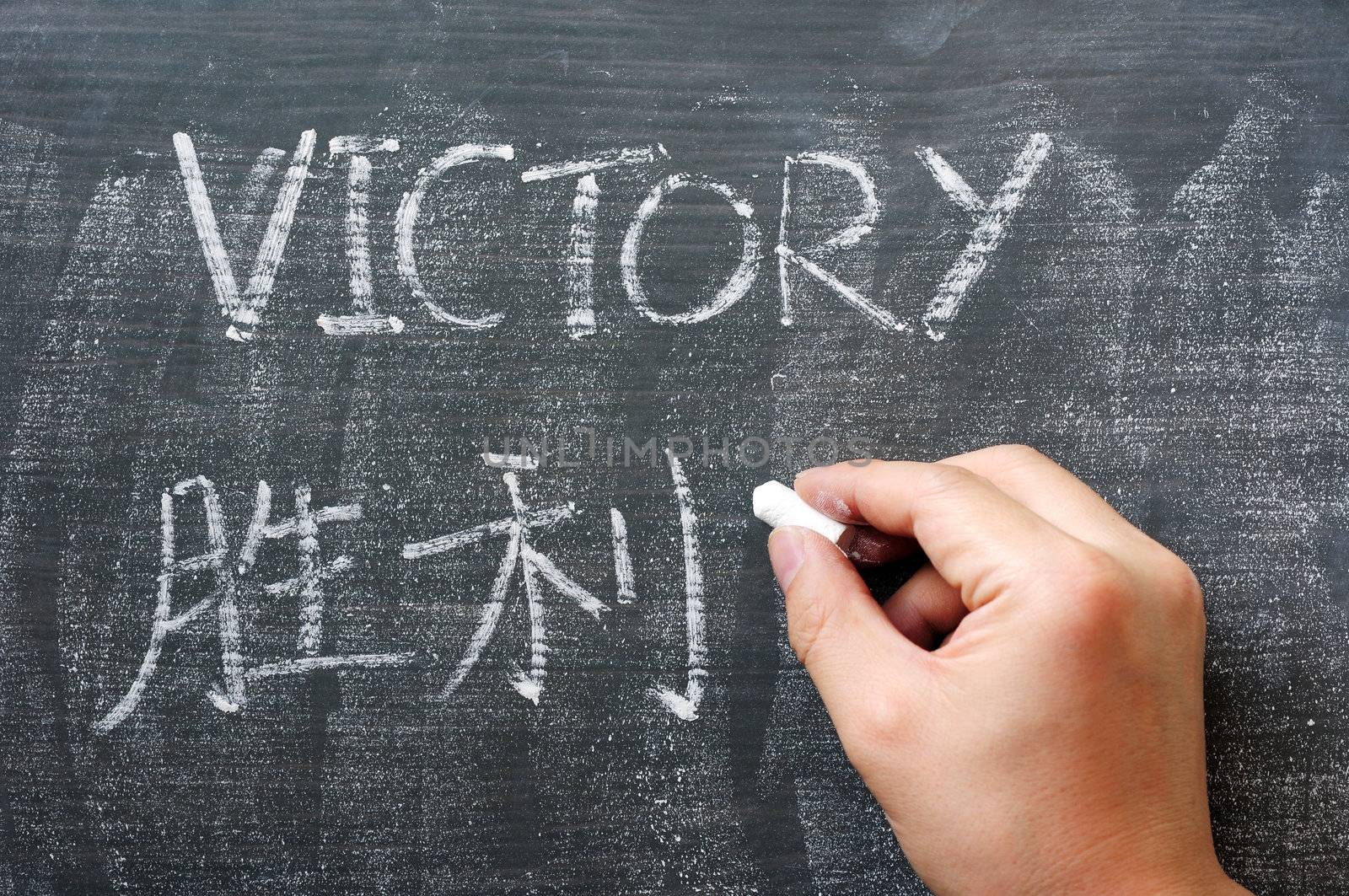 Victory - word written on a blackboard with a Chinese translation, with a hand holding chalk