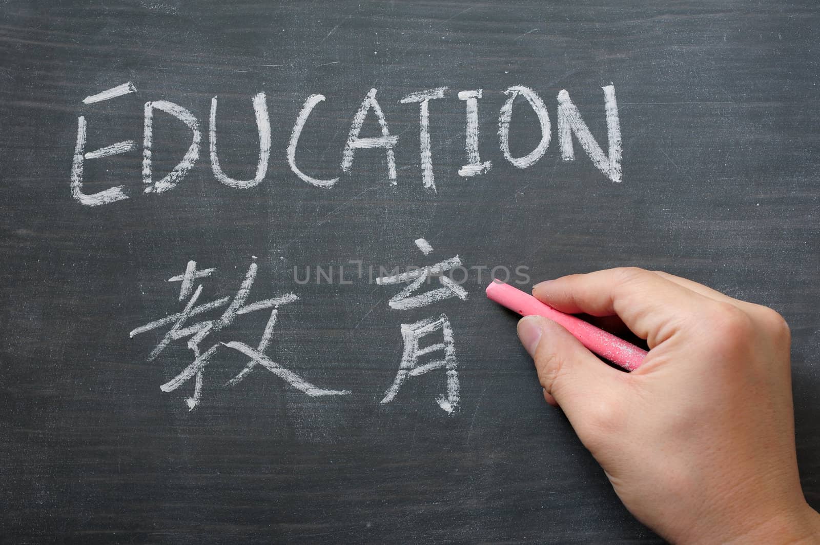 Education - word written on a smudged blackboard with a Chinese translation,with a hand holding chalk