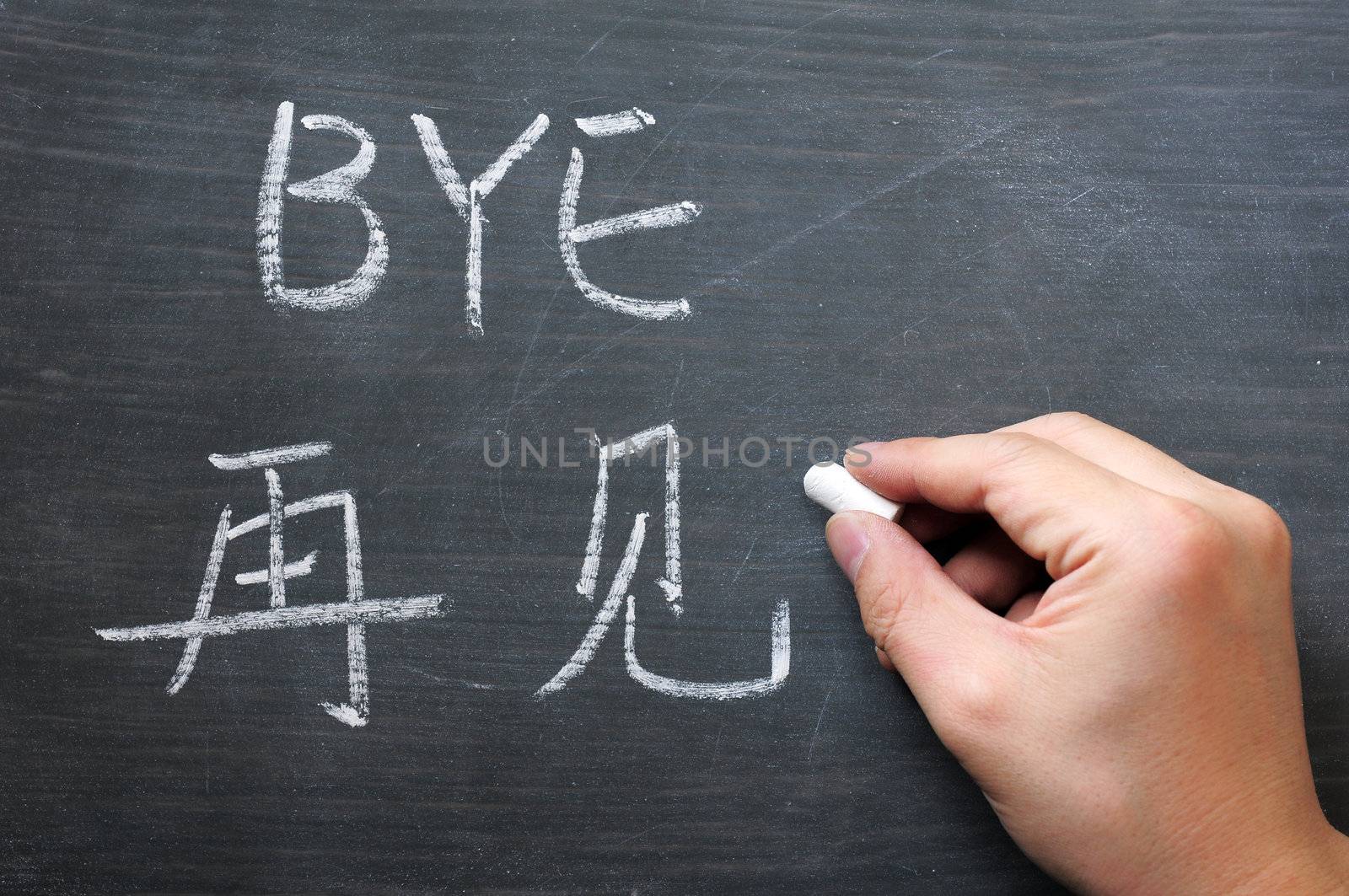 Bye- word written on a smudged blackboard with a Chinese translation, with a hand holding chalk