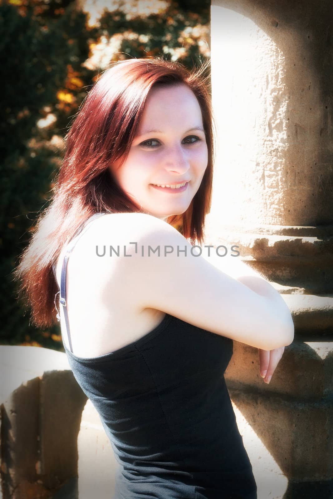 redhead woman lean to a stone column outdoor in a park