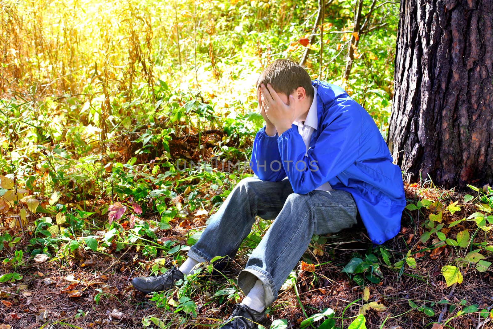 sad teenager sitting in the autumn forest alone