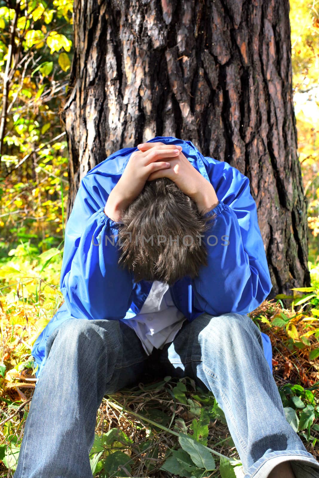 sad teenager sitting in the forest near the tree