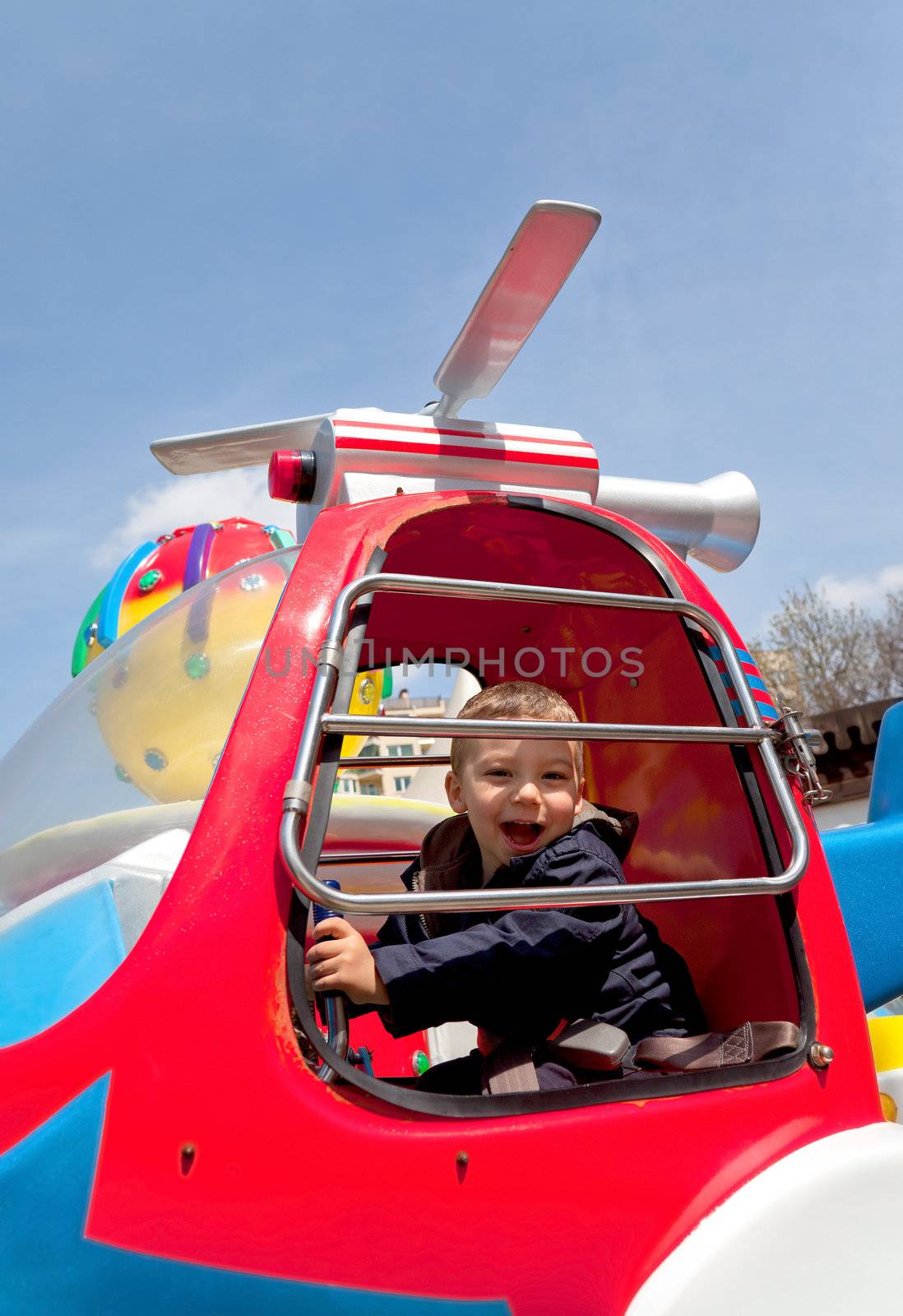 Sweet little boy riding carousel in toy chopper, smiling at camera