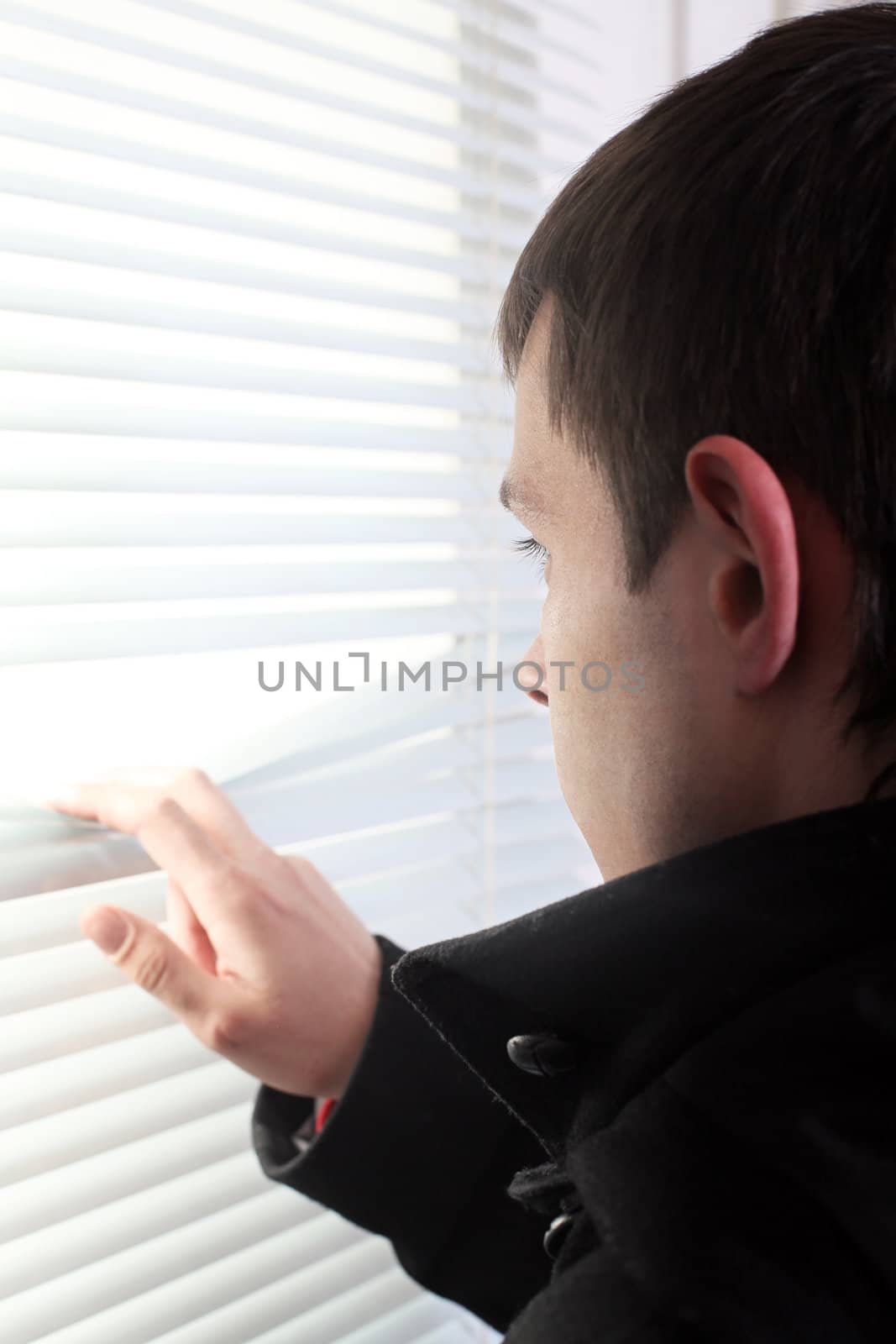 young man looking through the jalousie on the bright window