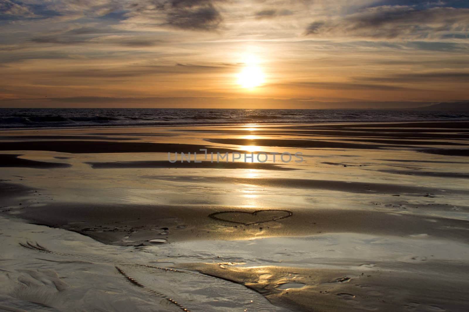 heart drawn in the wet sand on the beach at sunset