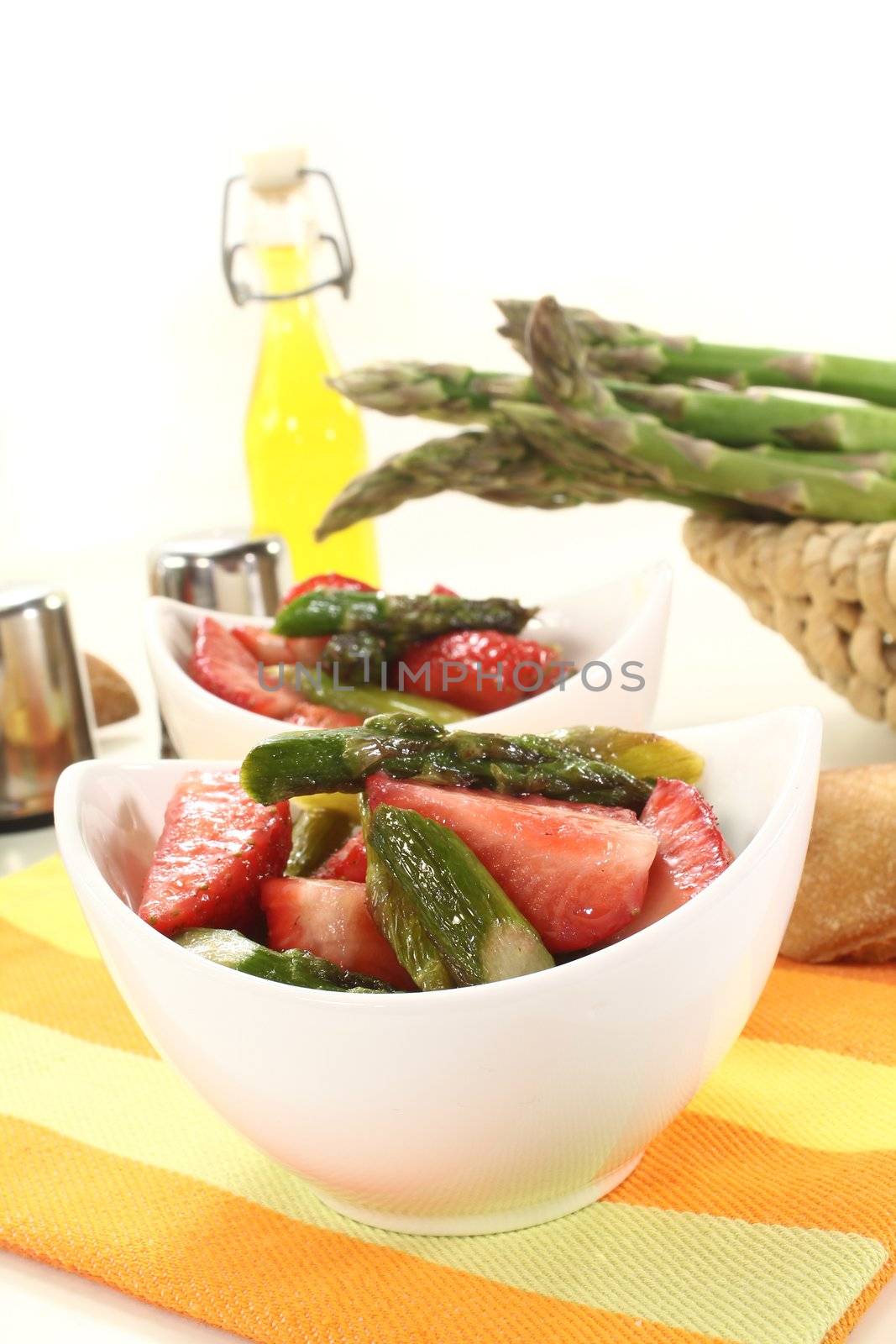 Asparagus salad with fresh strawberries and oil on a light background