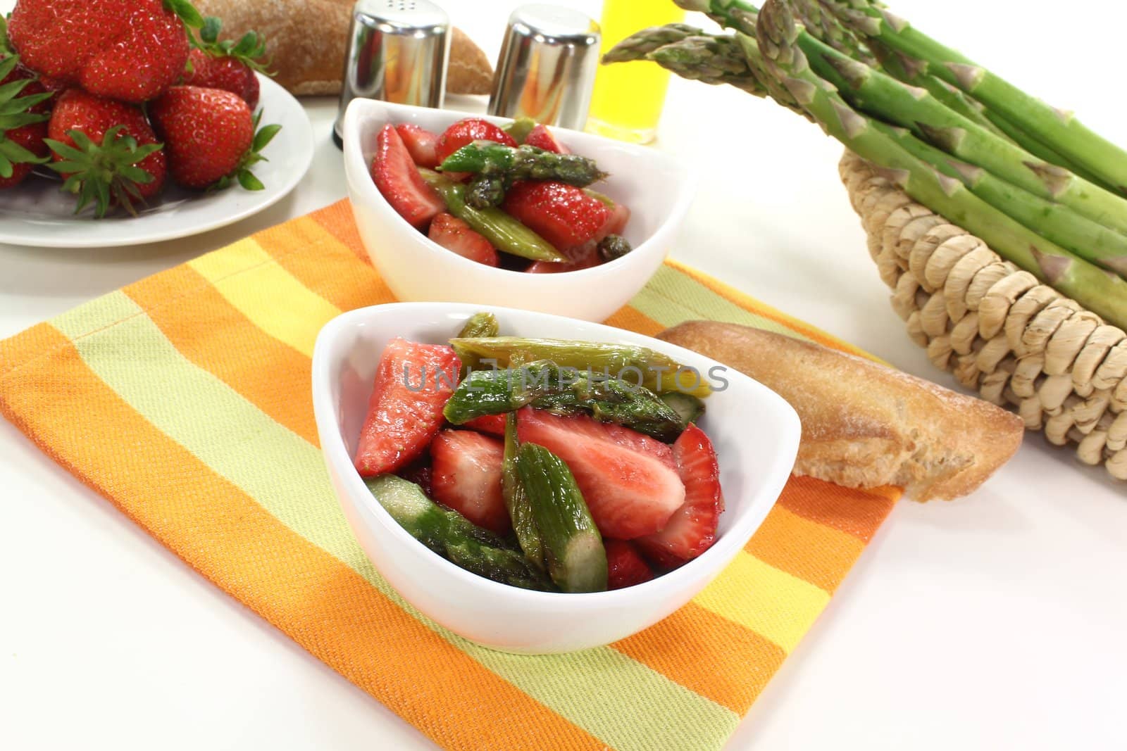 Asparagus salad with fresh strawberries, oil, and bread on a bright background