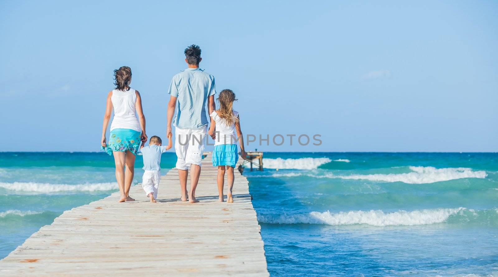 Family of four on wooden jetty by the ocean by maxoliki