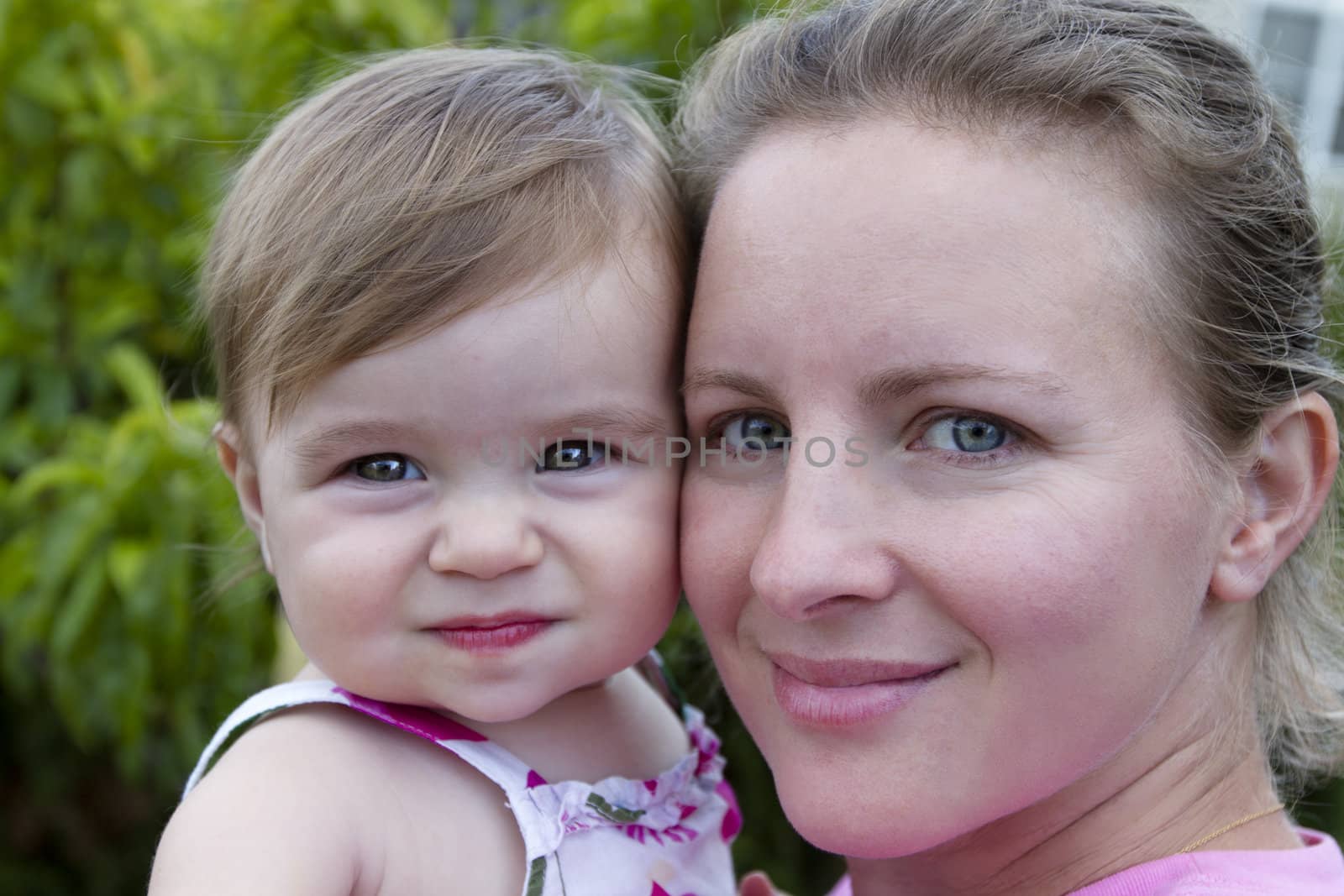 Mother and Daughter headshot. Mother looking at camera with a secure, trusting feelings. Smilar impression on 11 months baby.