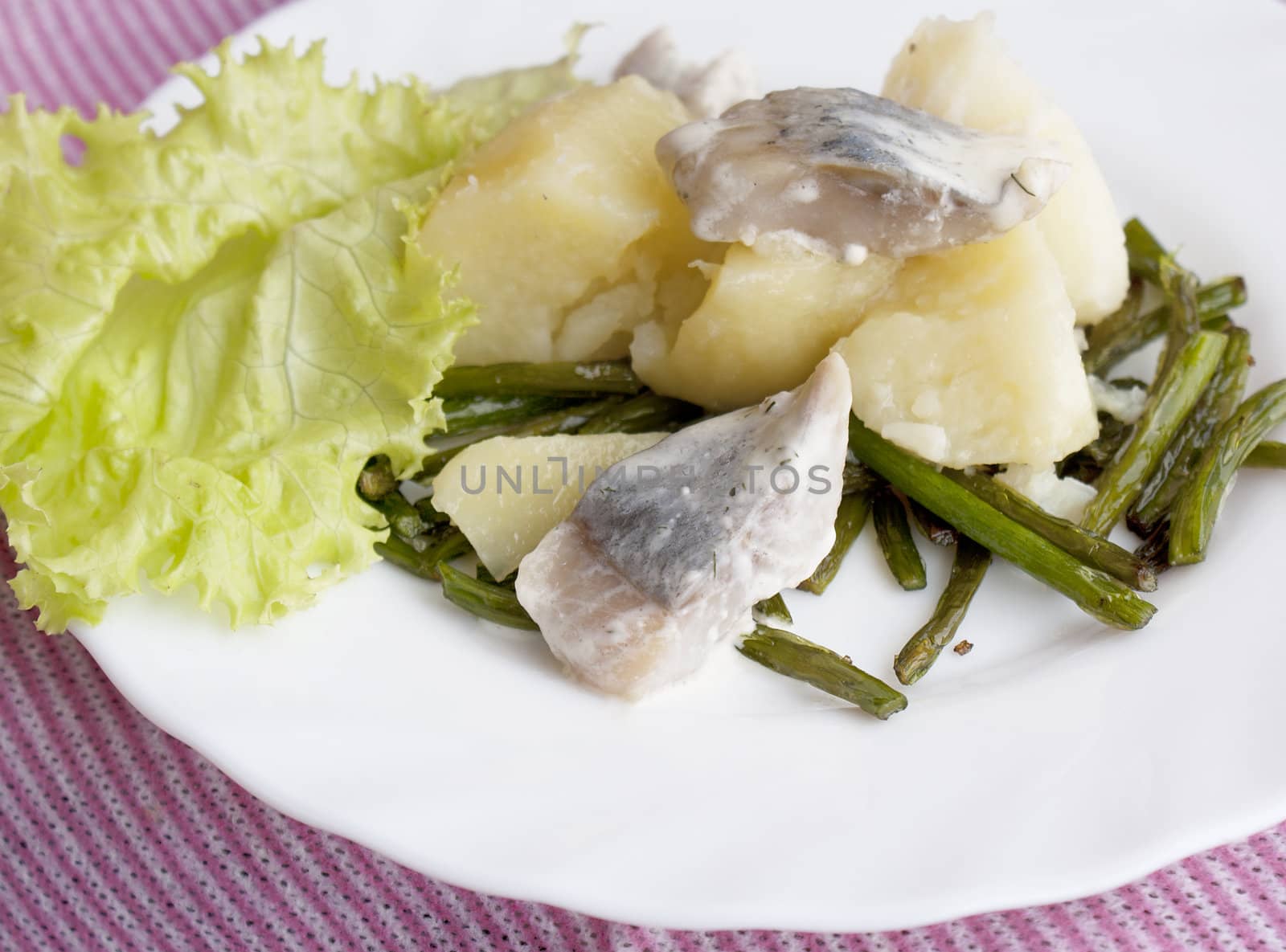 Appetizing marinaded herring with a boiled potato and fried stalks of garlic