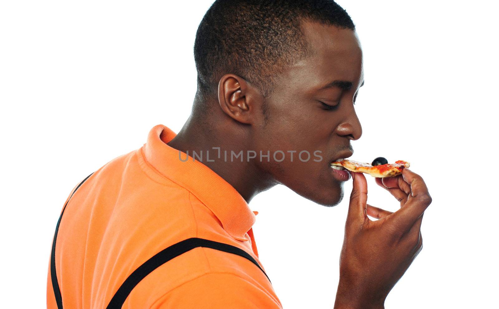 Young man eating a slice of pizza by stockyimages
