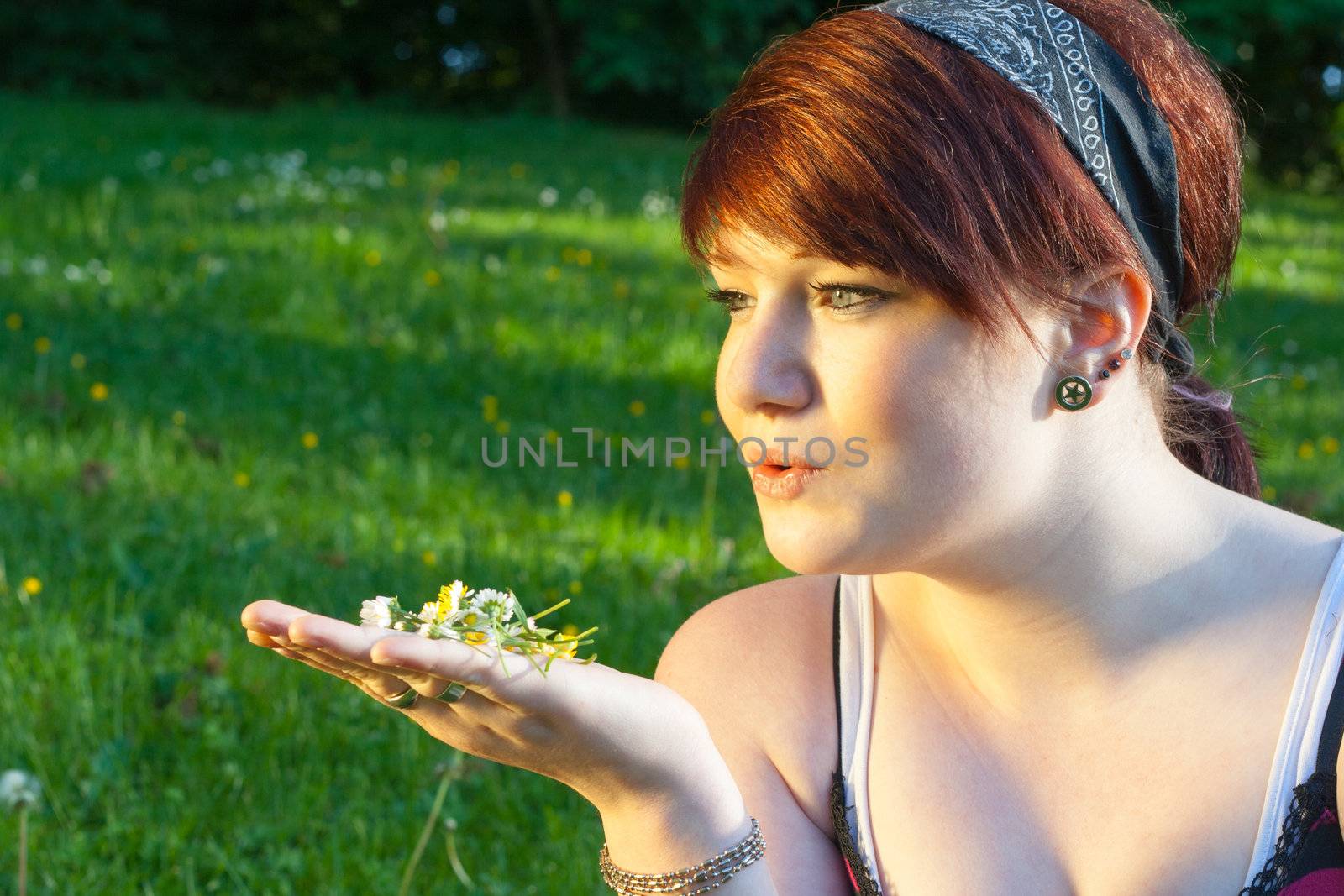 A beautiful young girl lying on the grass with some Daisys in her hand on a background of green