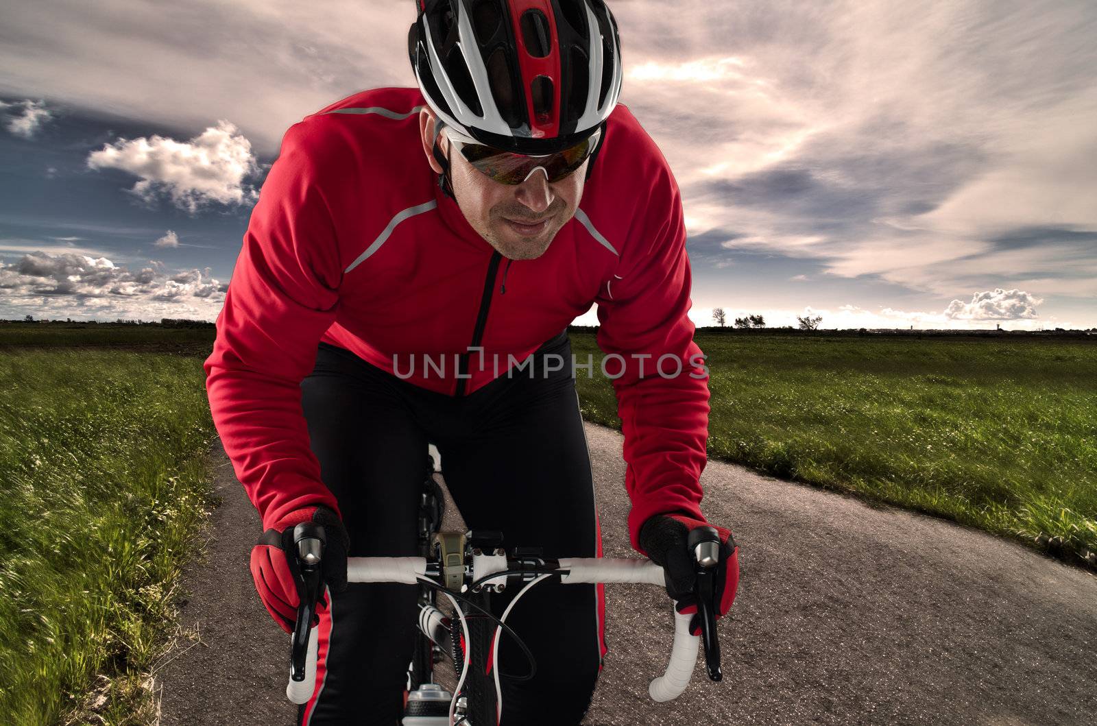 Cyclist on road bike through a asphalt road and blue sky with clouds.