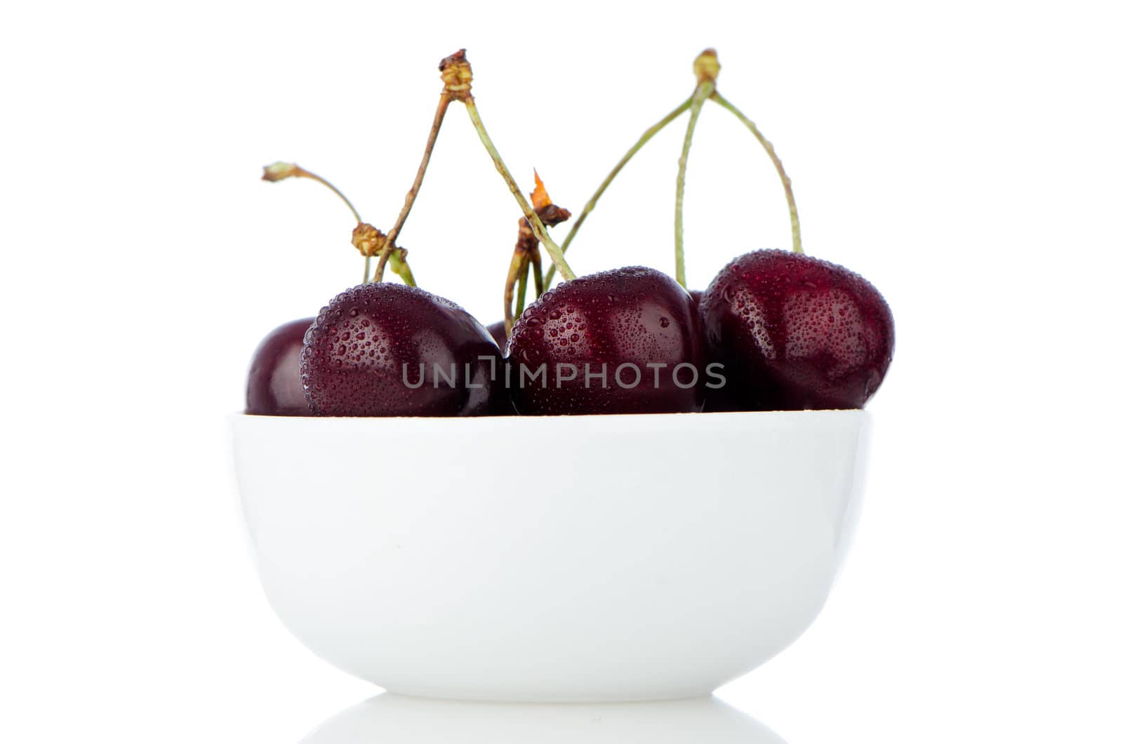 Cherry in white bowl on white reflective background.