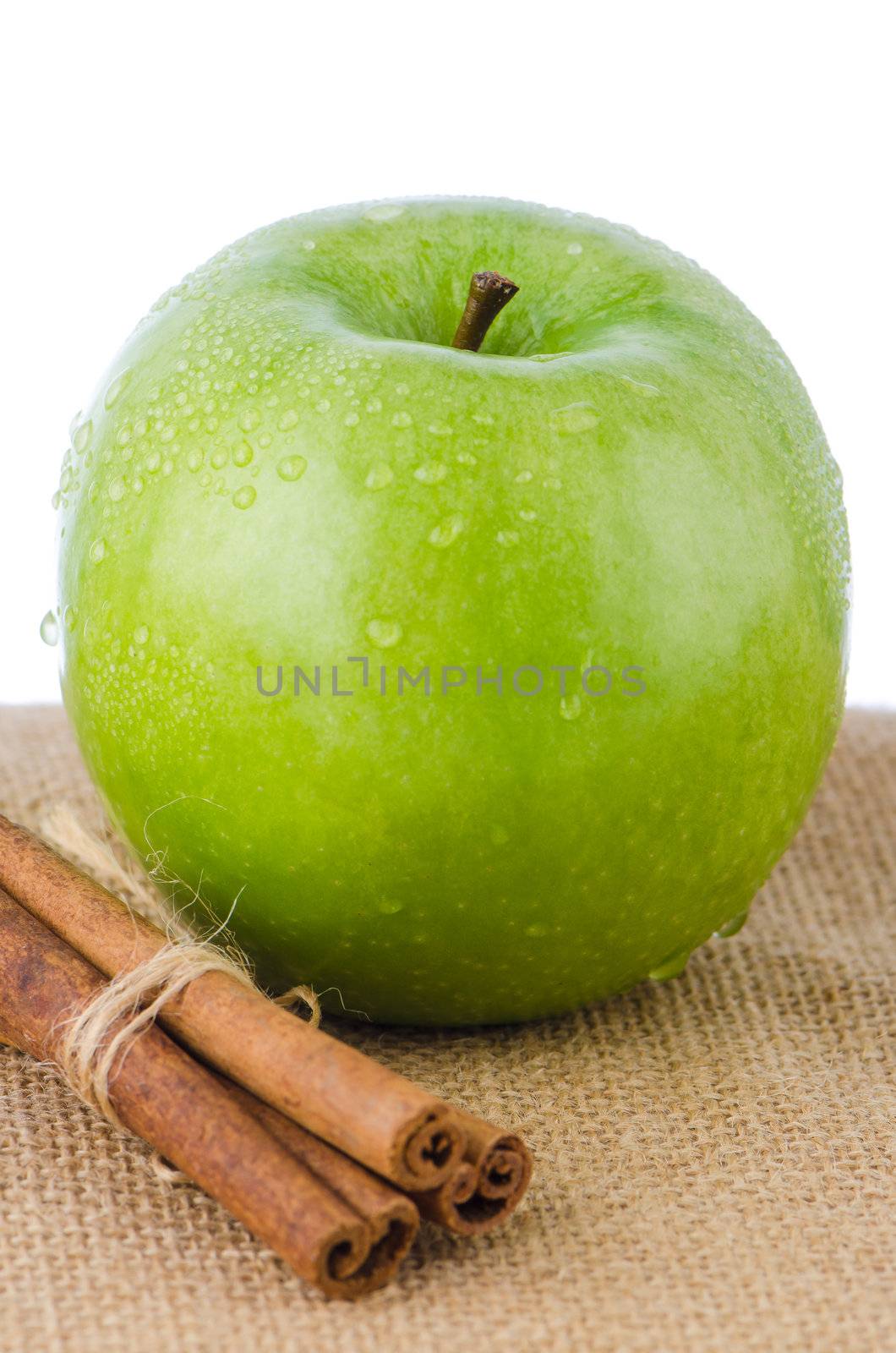 Ripe green apple with cinnamon sticks over rafia on white background