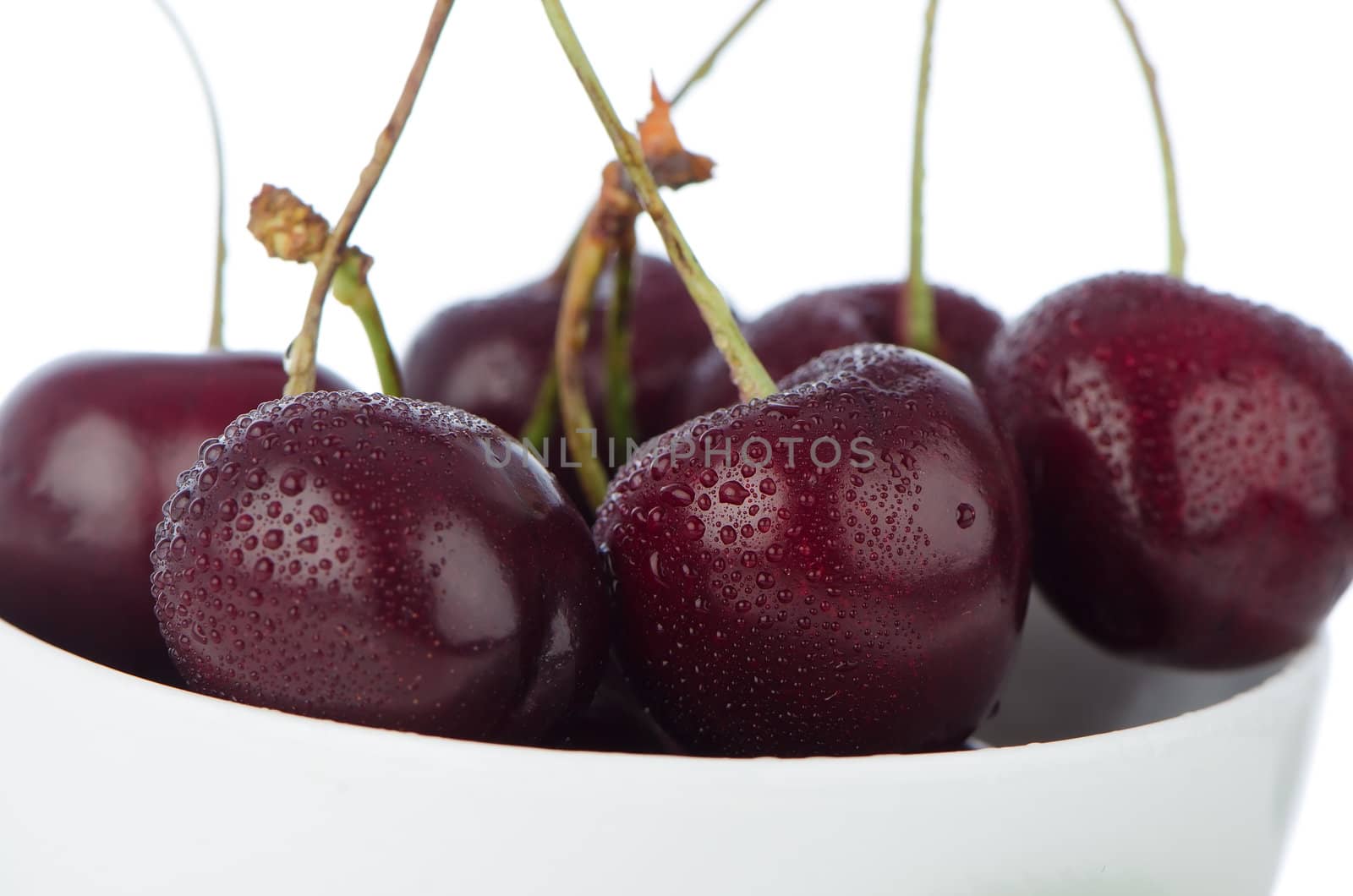 Cherry in white bowl on white reflective background.