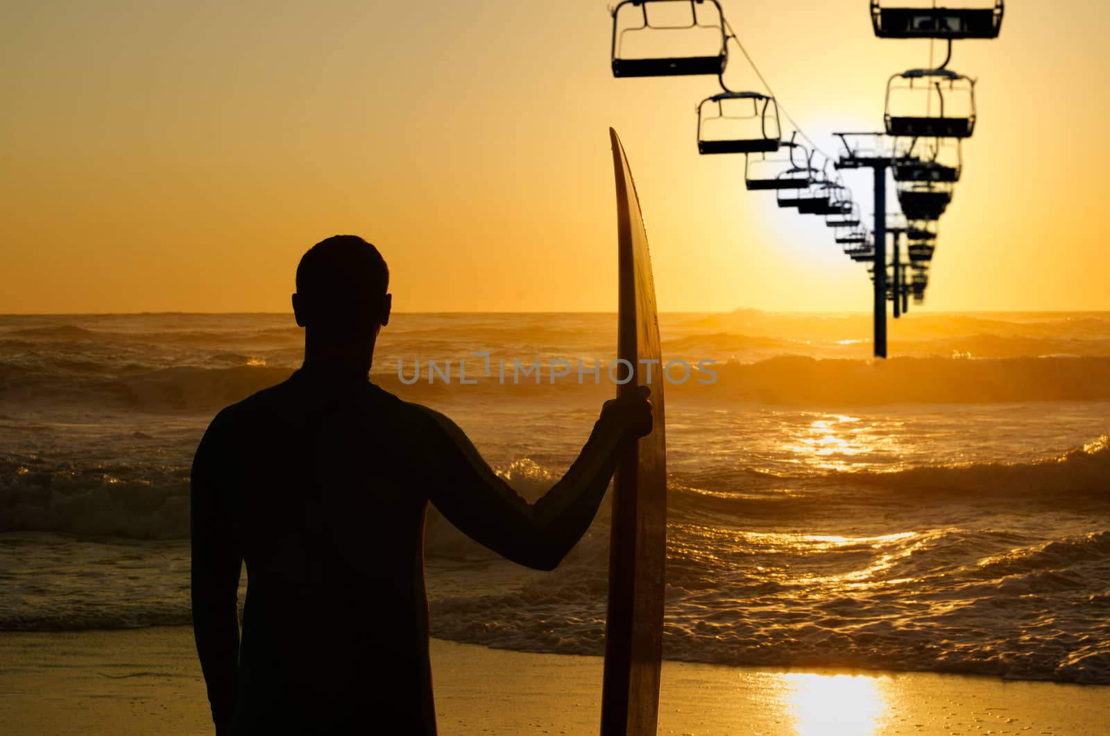 Surfer watching the ocean waves and a chair lift  transport system at sunset.