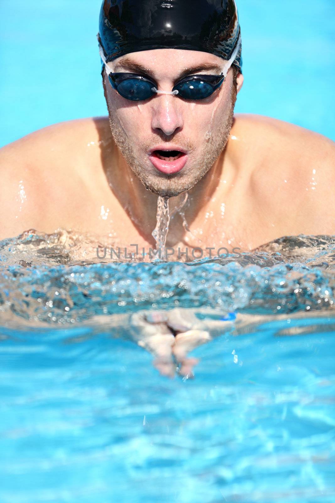 Swimmer - man swimming breaststroke. Male sport fitness model doing breast swimming in pool wearing swimming goggles and swim cap.