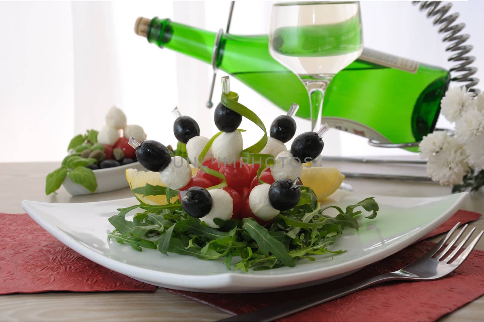 Mozzarella with cherry tomatoes and olives on a skewer with arugula and white wine