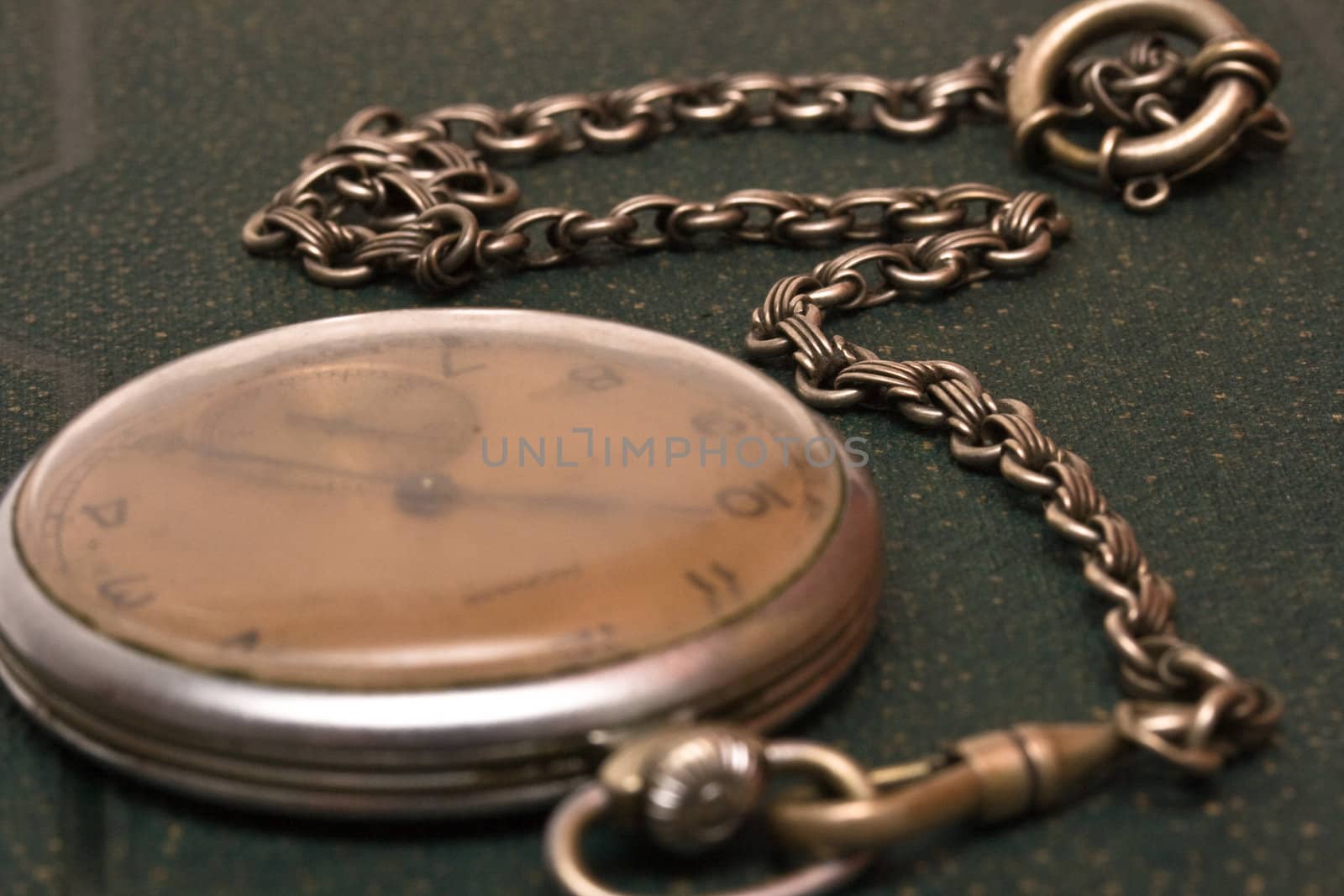 Very old clock with chain lying on rough green  surface - shallow depth of field