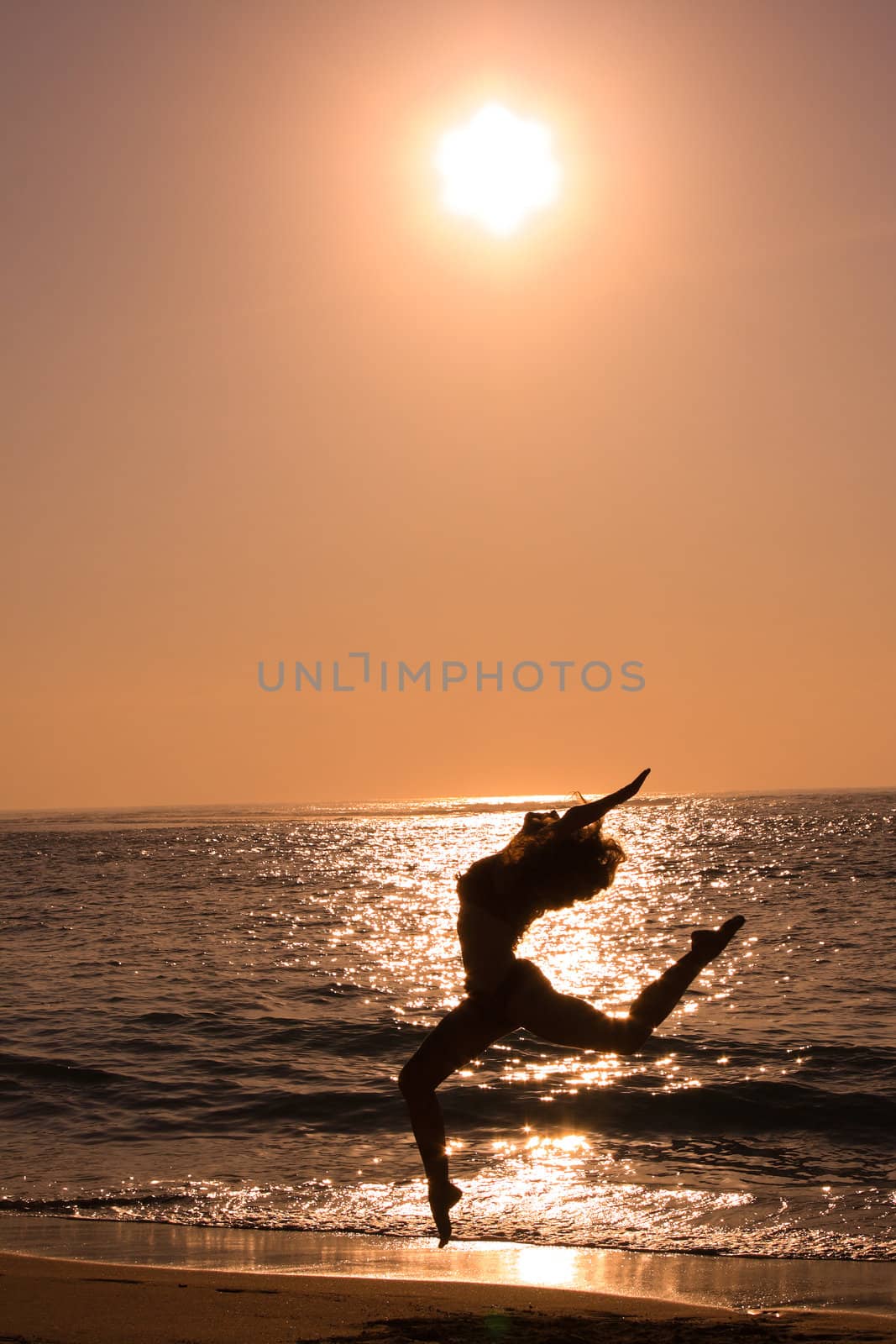 Female jumping at beach on sunrise by dimol
