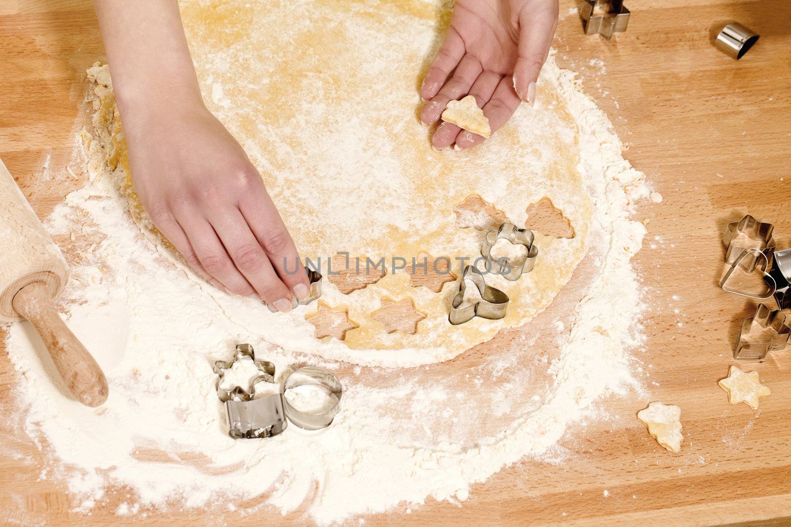 closeup of hands pressing christmas molds in dough on a kitchen table