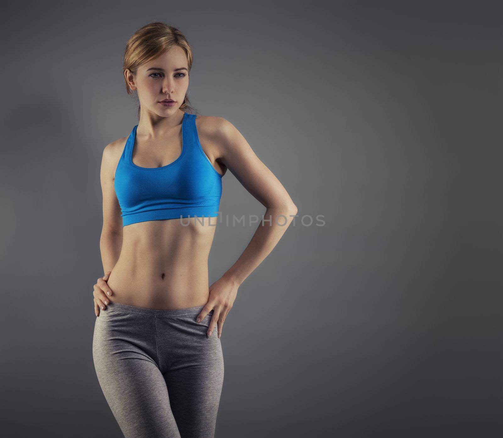 young beautiful woman in fitness dress standing in front of grey background