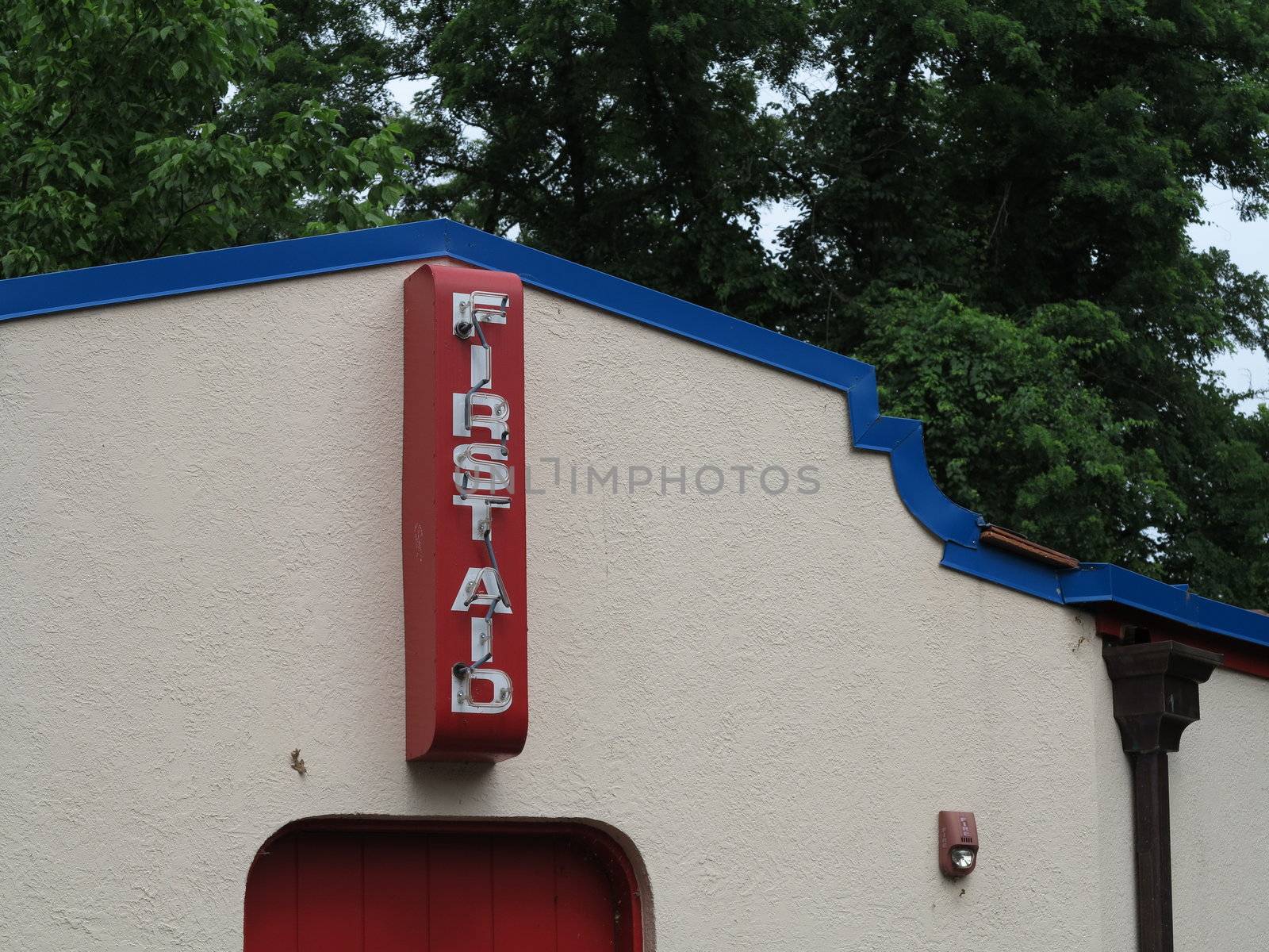 Red and white first aid sign with neon lighting on side of old building