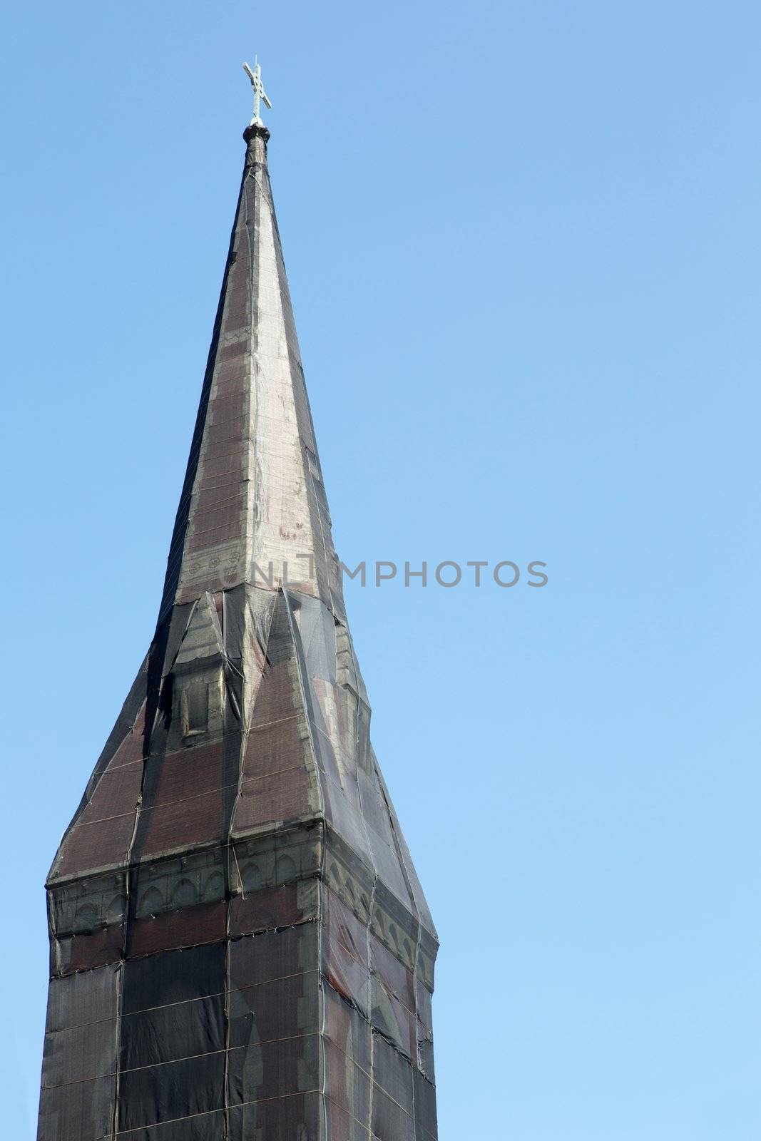 Curious black net shrouded Christian church steeple against blue sky