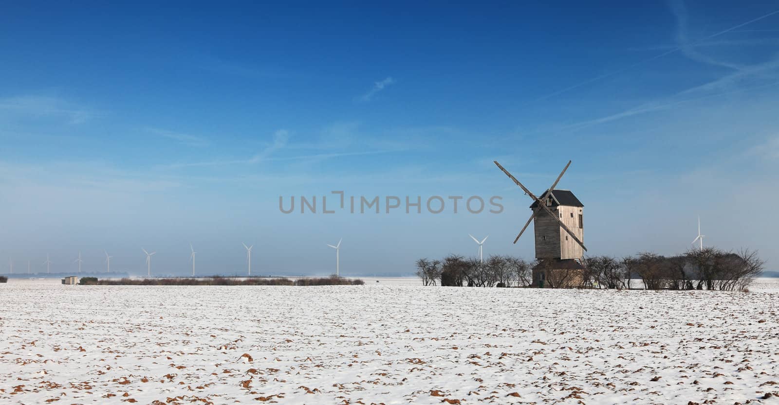 Winter landscape in the central region of France, with a traditional wooden windmill and some modern windturibines in the distance.
