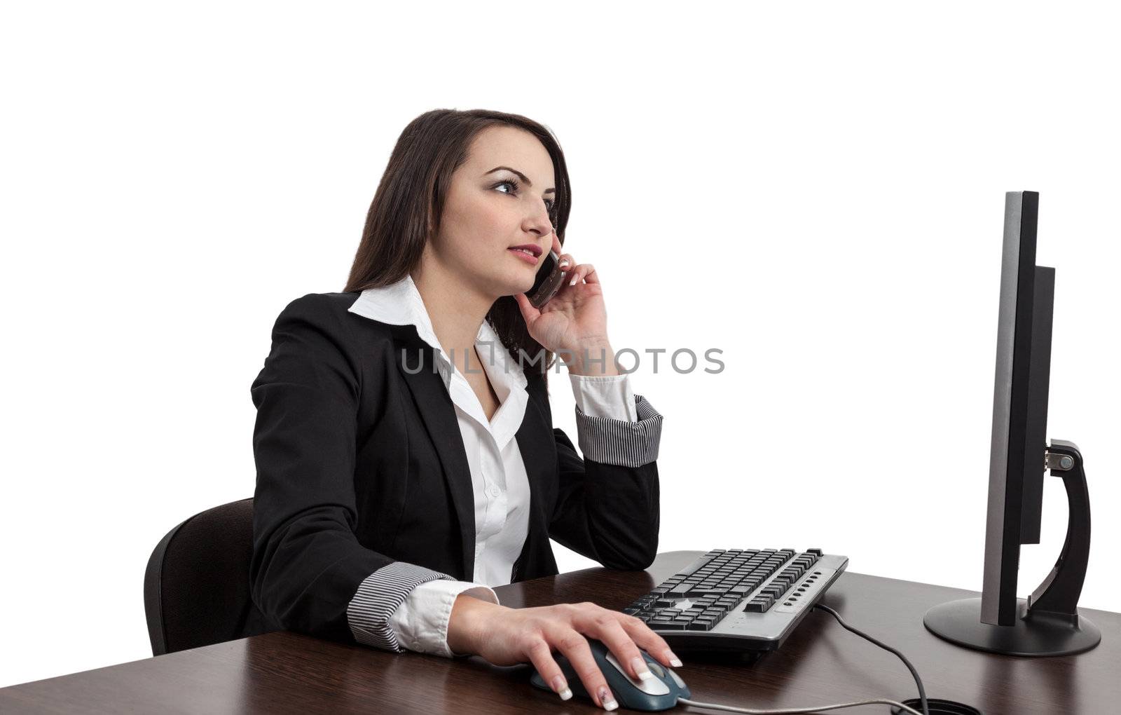 Image of a young brunette woman working on a computer and using a mobile phone , isolated against a white background.