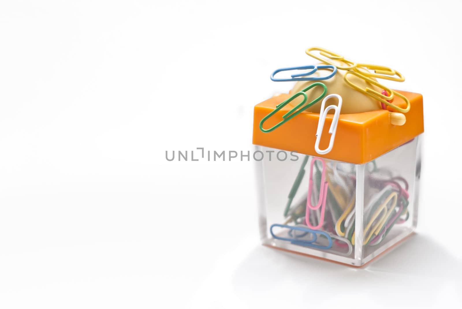 Colorful plastic coated paper clips in clear innovative container with magnet, isolated on white background