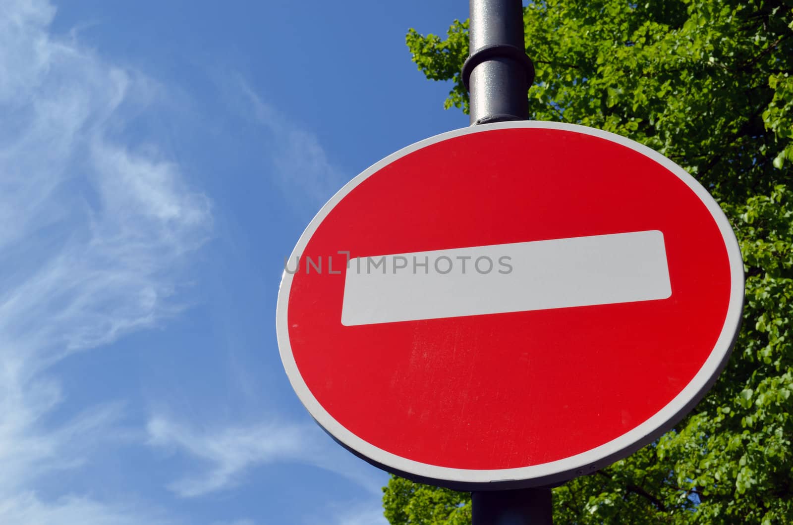 Limiting traffic sign white brick on red round background against blue sky and green trees.