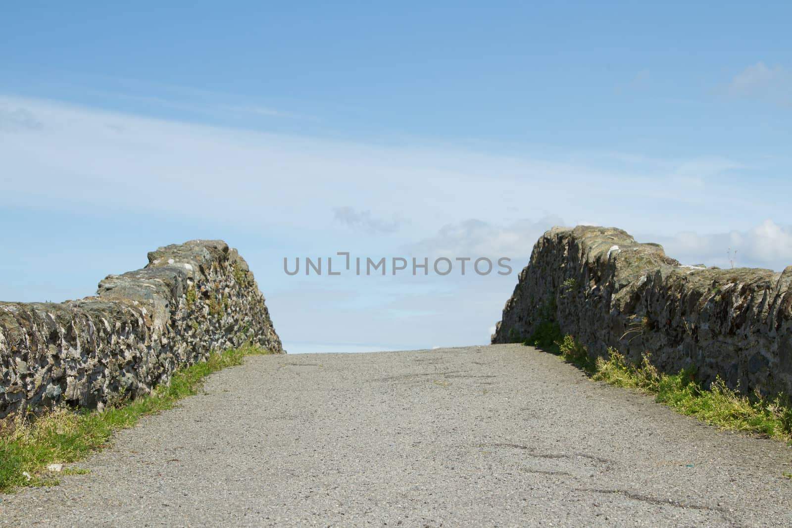 An old bridge rises up with stone walls to the horizon beyond with a blue cloudy sky.