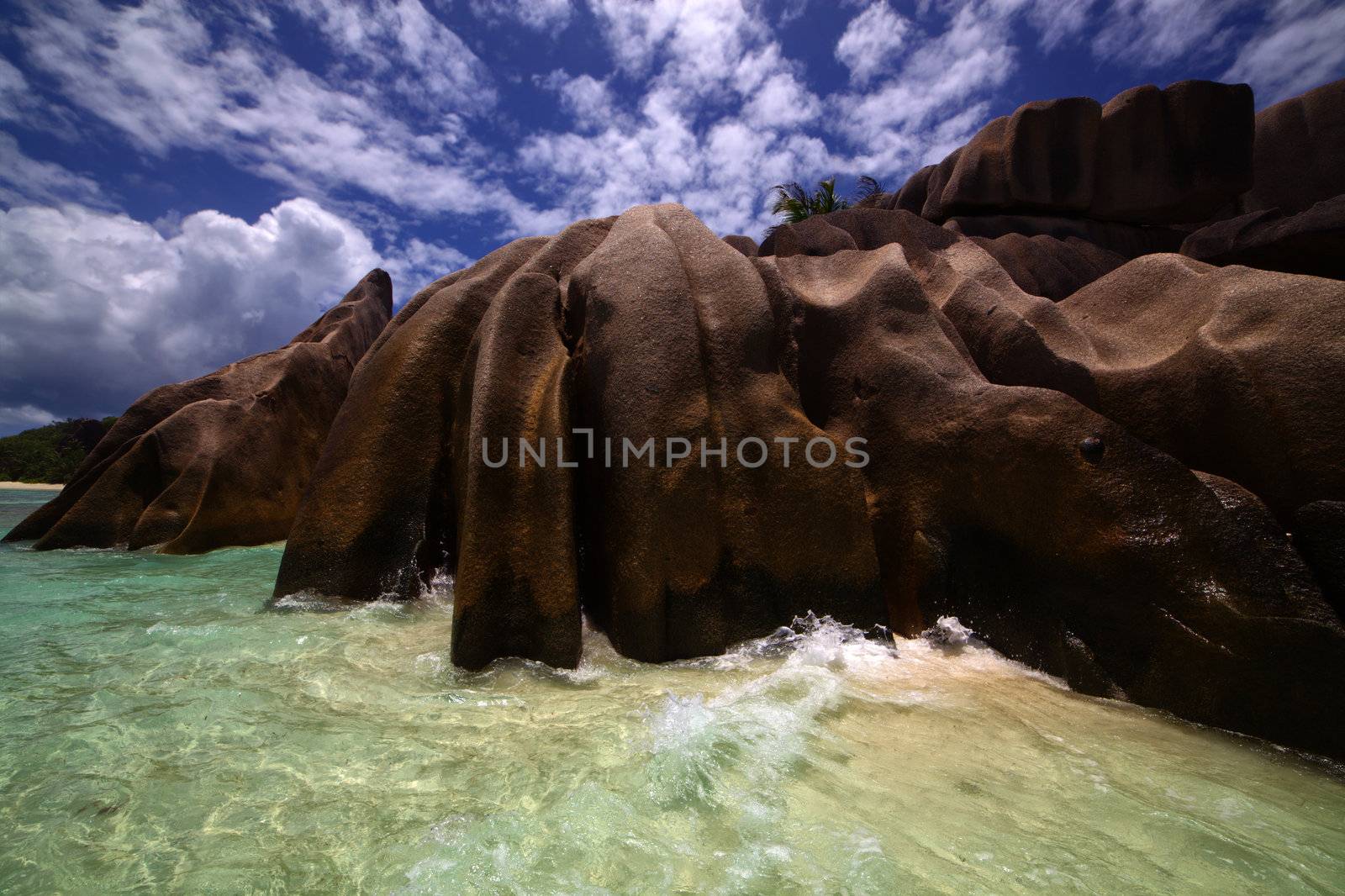 Blue sky laced with fluffy white clouds over a beautiful shore lined with smooth weather worn boulders