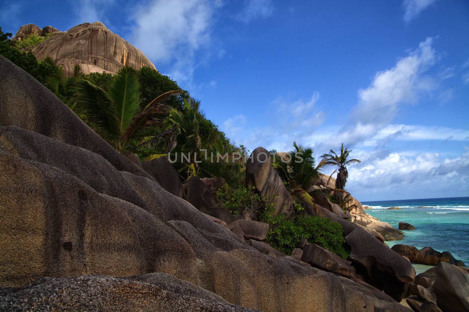 Steep rocky shoreline leading to the ocean beach under a tropical sky