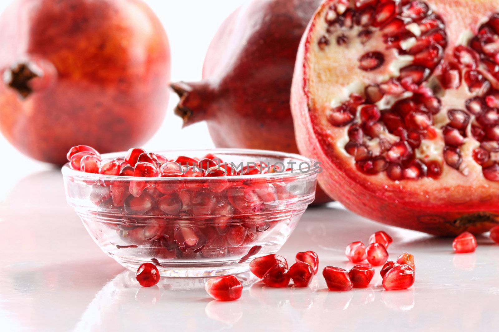 Ripe pomegranates and glass bowl of seeds on white by Sandralise