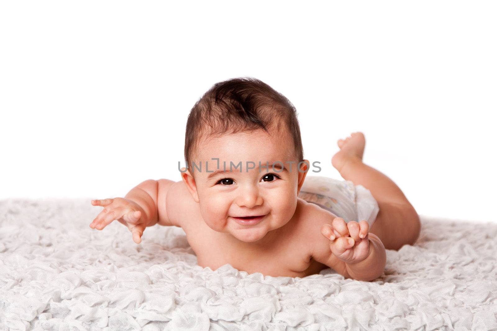 Cute happy smiling baby laying on belly on soft surface wearing diaper, looking at camera, isolated.