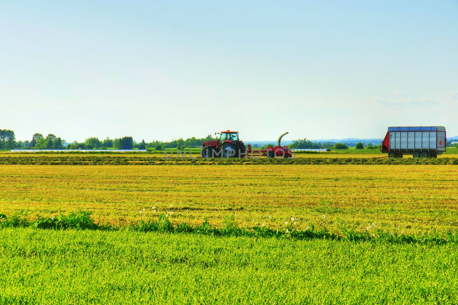 Beautiful HDR rendering of rural landscape with early farm work in the cereal field with tractor and other equipment.