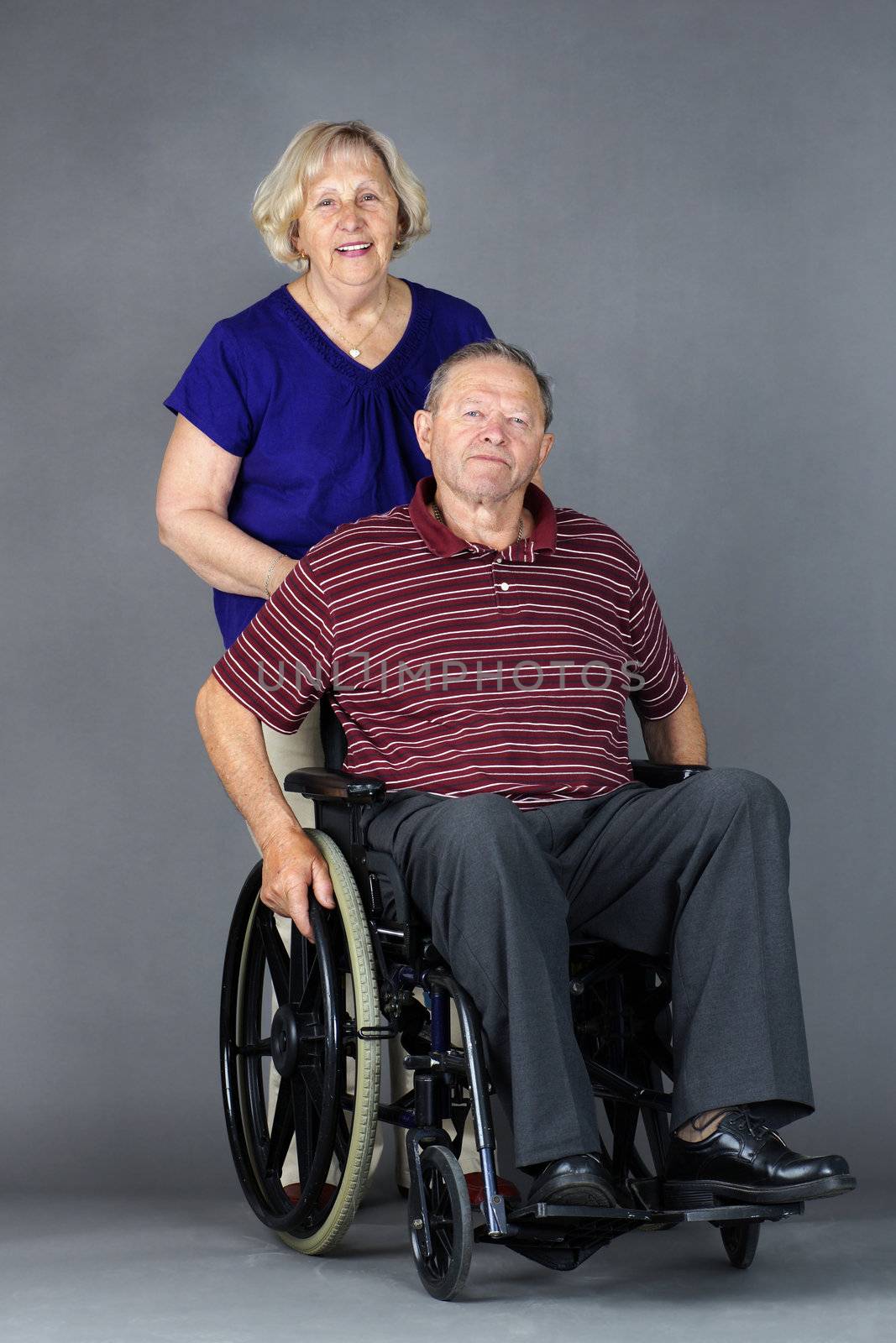 Happy senior couple with old man in a wheelchair, studio shot on grey.