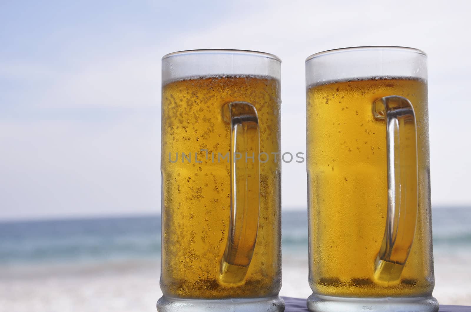 Two mugs of chilled Beer on a sunny day at the beach