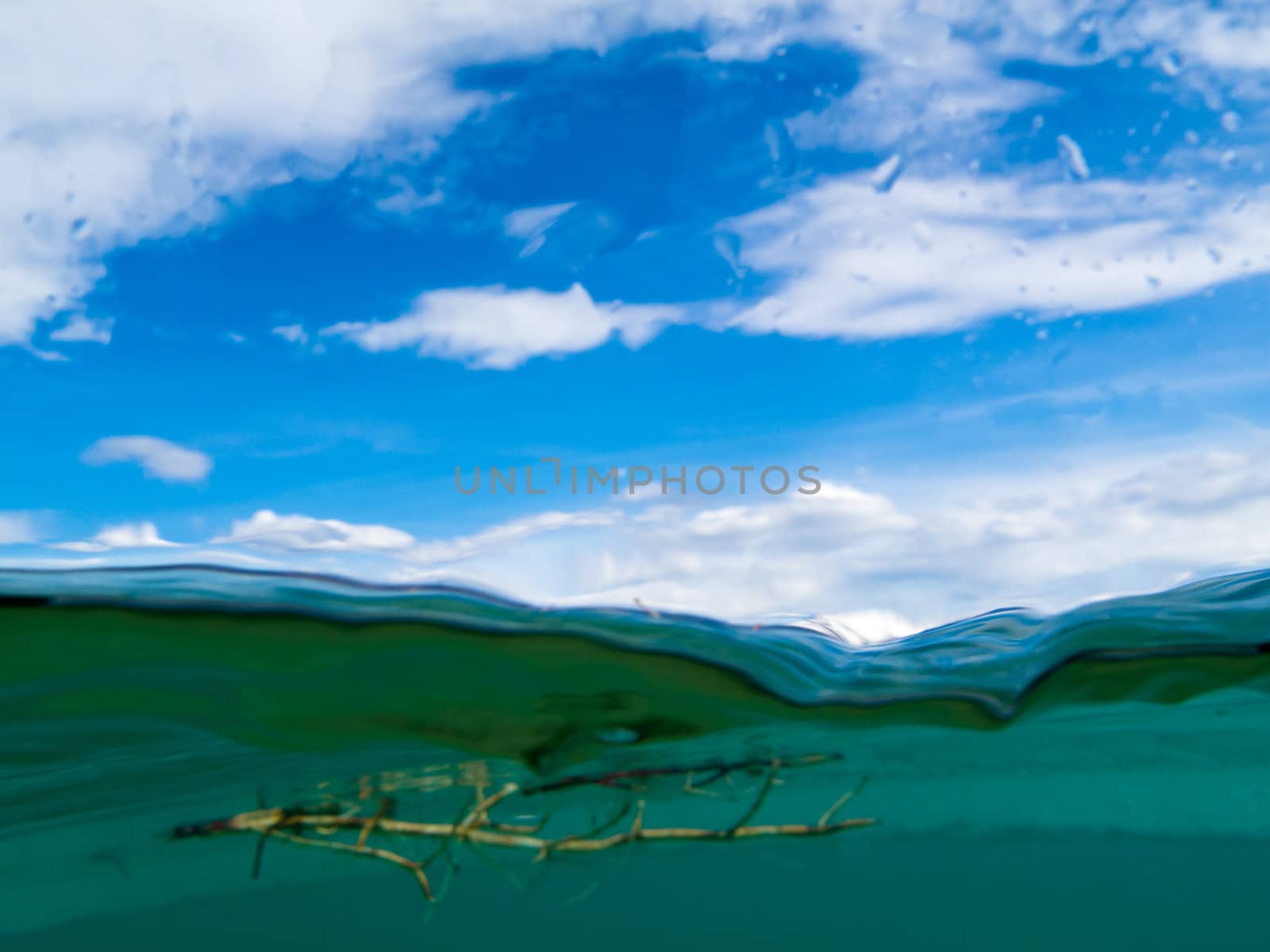 Underwater view: Breaking trough the surface into the air with blue sky and clouds.