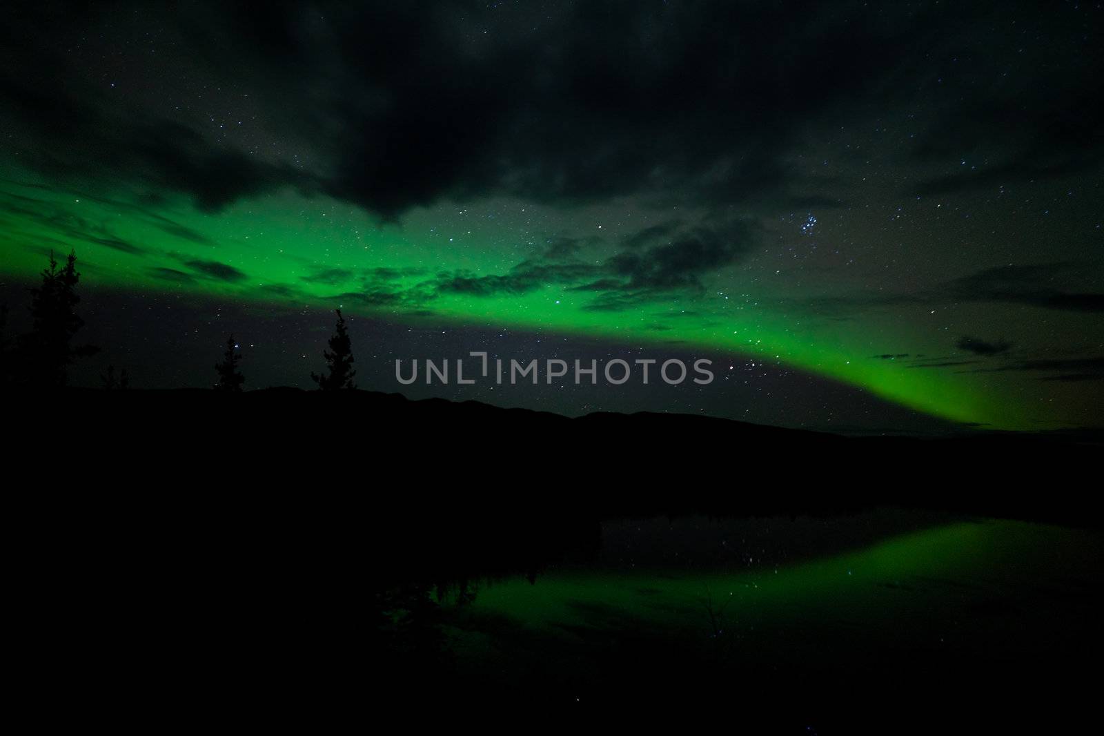 Night Sky Stars, clouds and Northern Lights mirrored on calm lake in Yukon, Territory, Canada.