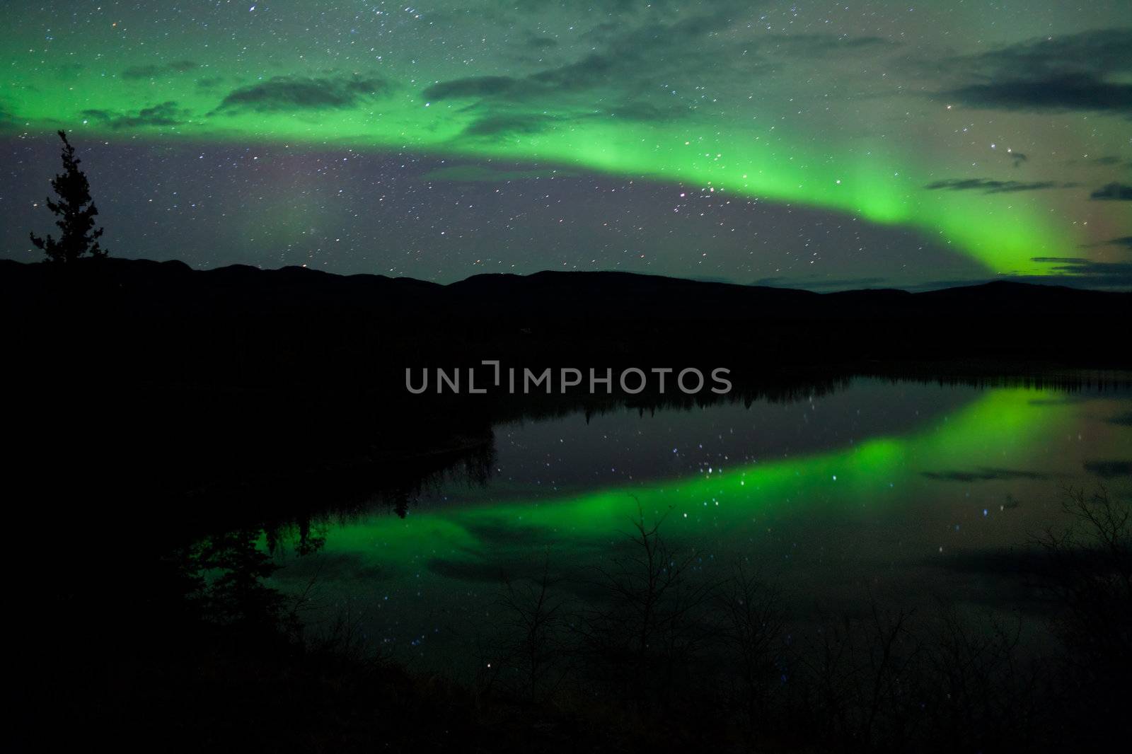 Night Sky Stars, clouds and Northern Lights mirrored on calm lake in Yukon, Territory, Canada.