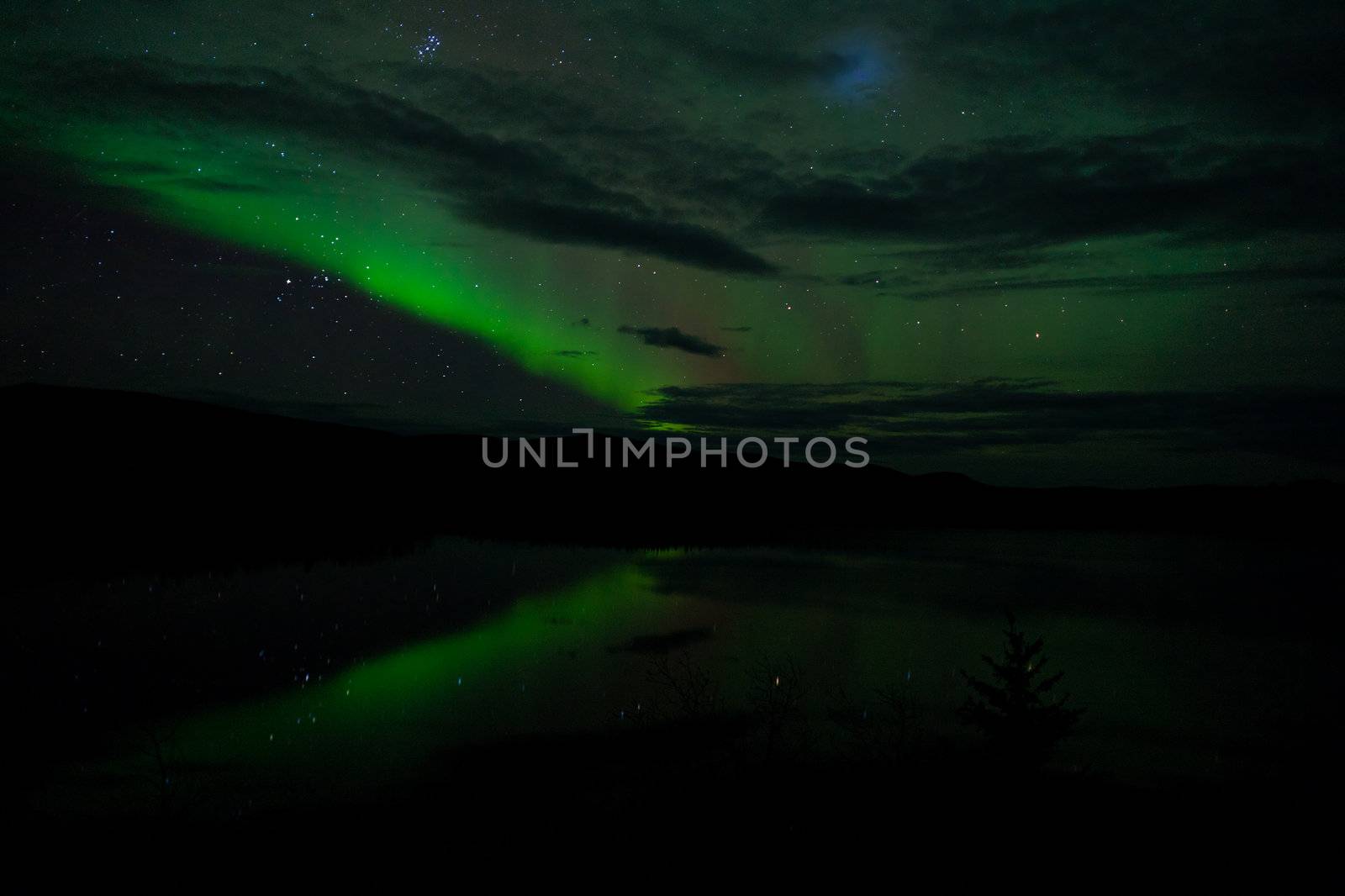 Night Sky Stars, clouds and Northern Lights mirrored on calm lake in Yukon, Territory, Canada.