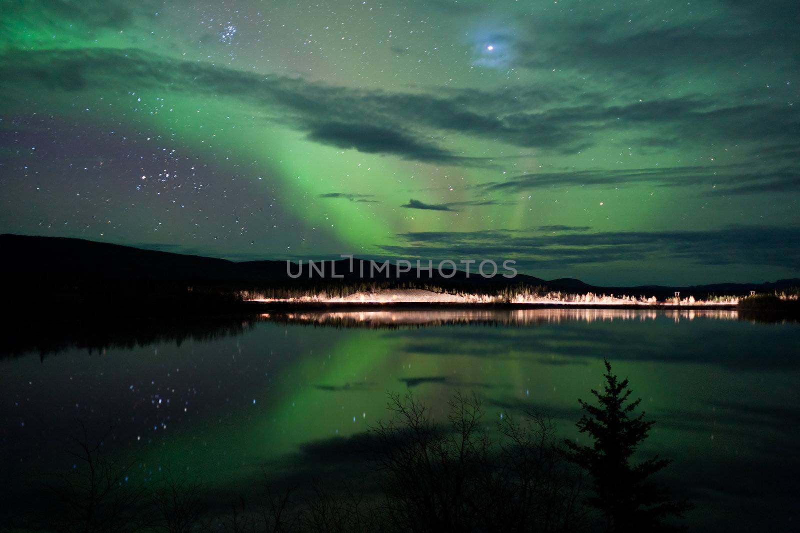 Night Sky Stars, clouds and Northern Lights over country road at lake shore, Yukon, Territory, Canada.